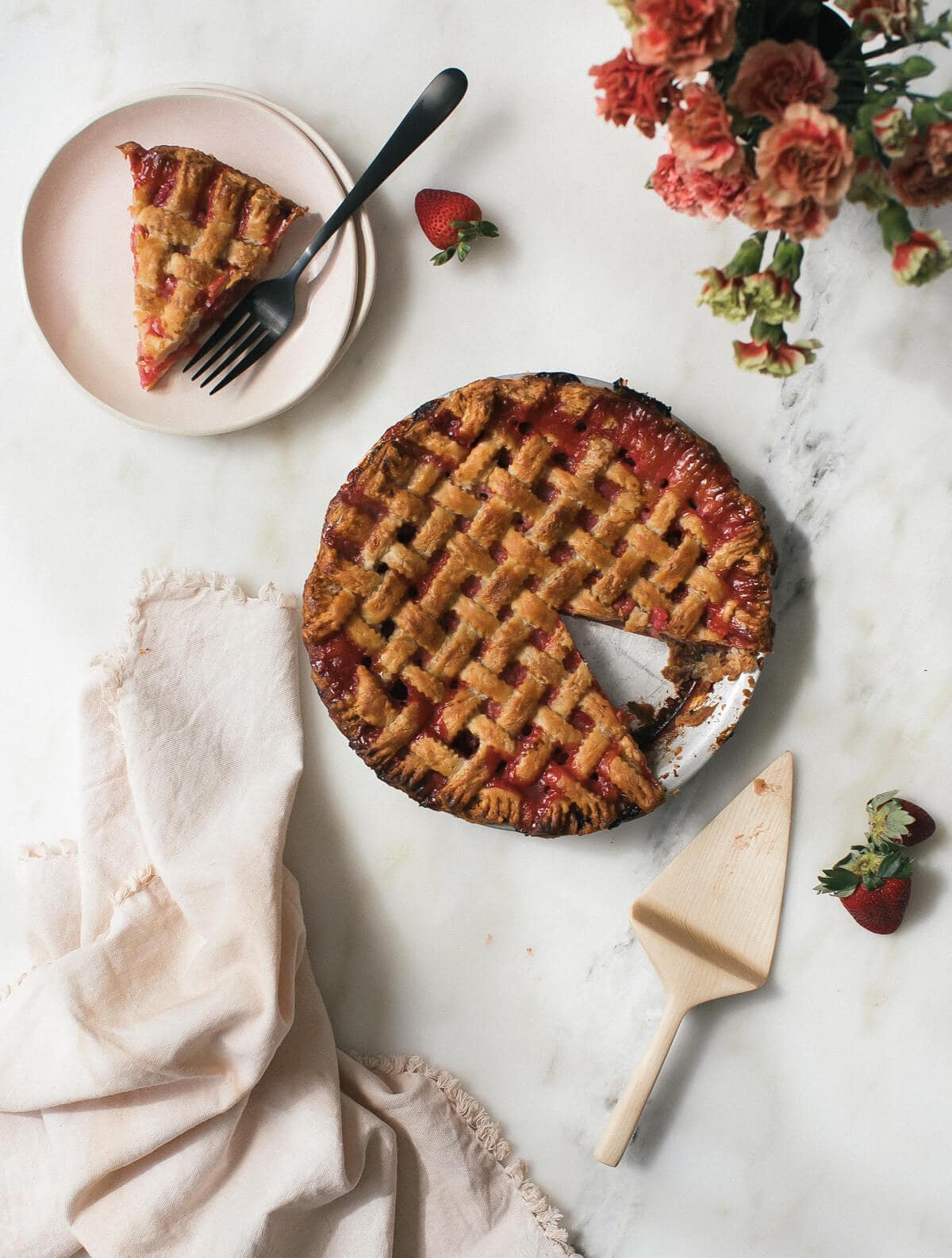 Rhubarb strawberry pie on a counter with a slice of pie on a plate near by.