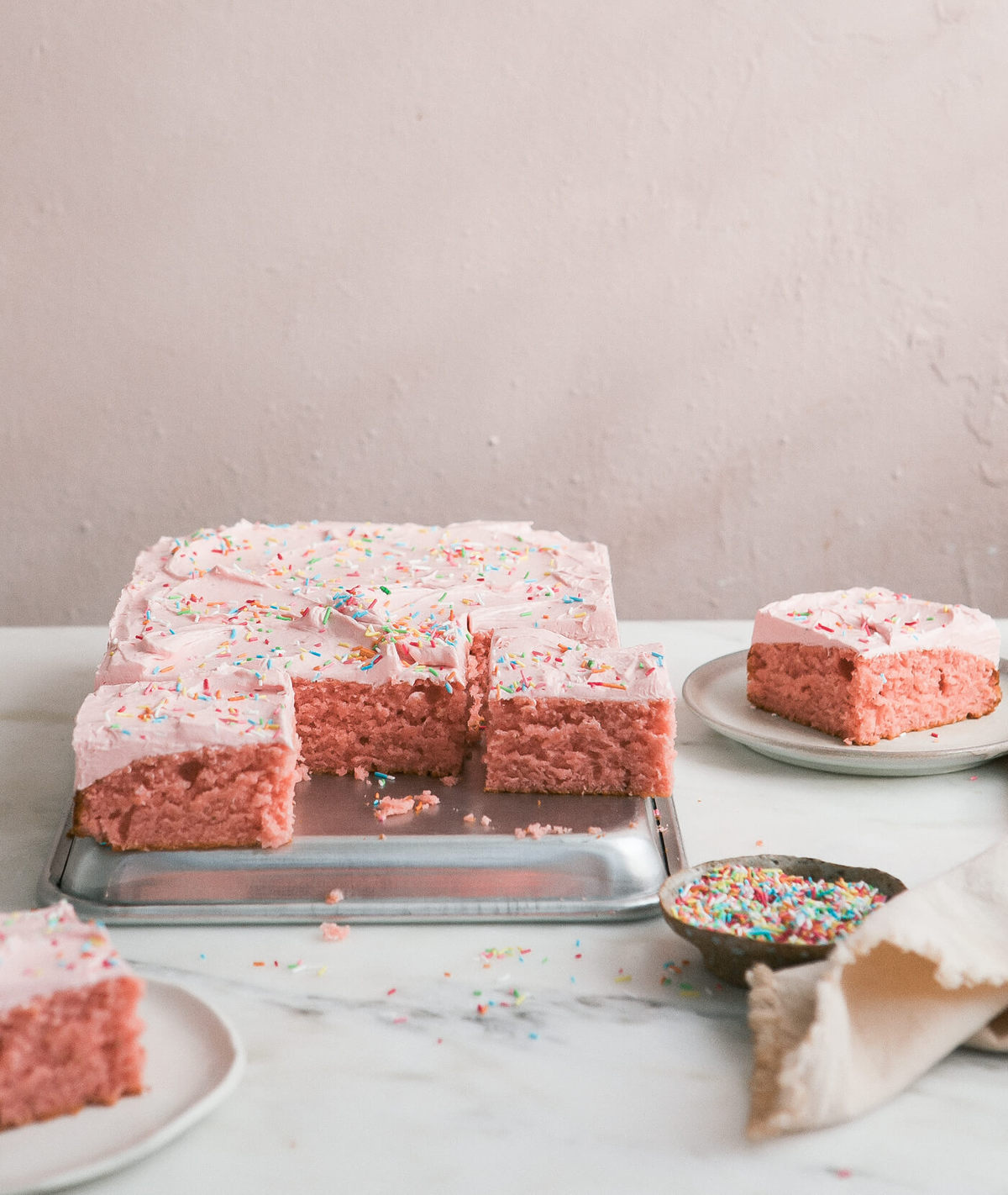 3/4 image of a sliced strawberry sheet cake with rhubarb frosting sitting on top of an overturned sheet pan.