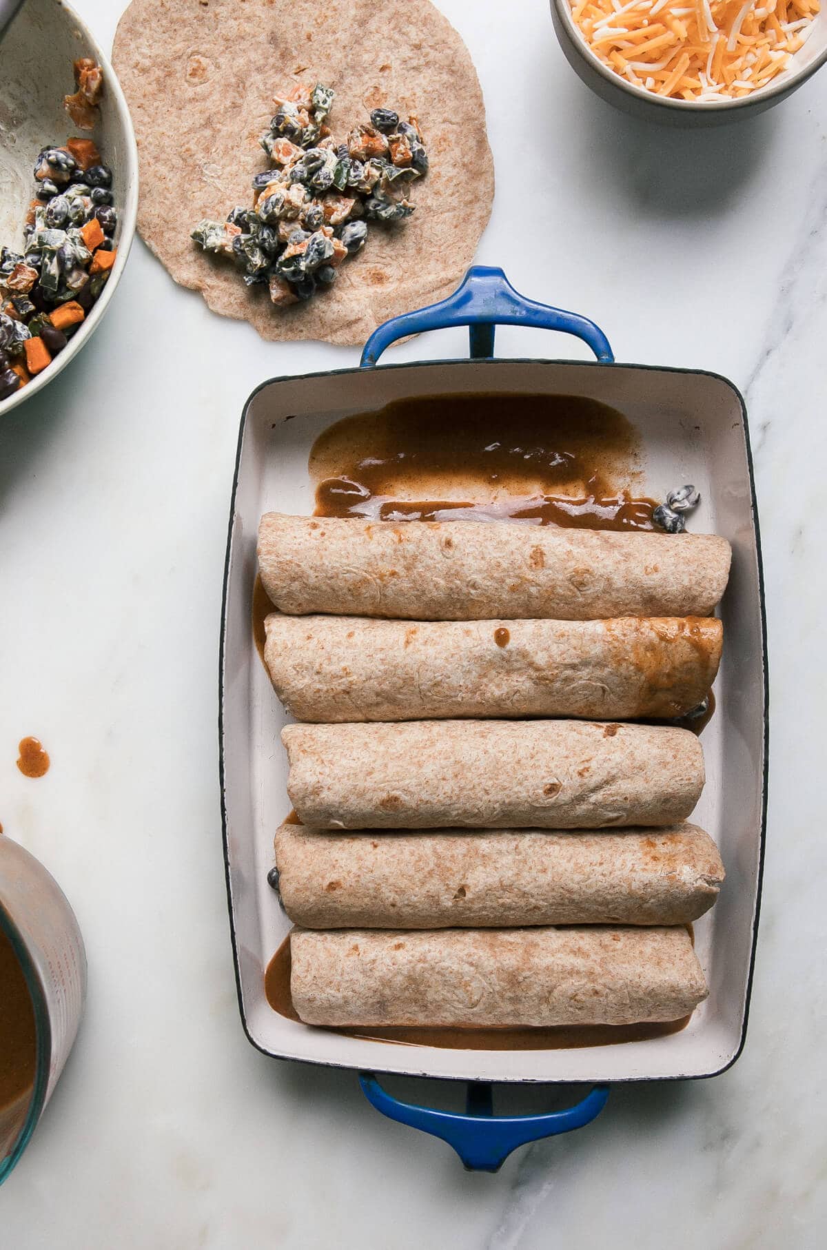 Rolled up tortillas stuffed with filling in a baking dish.