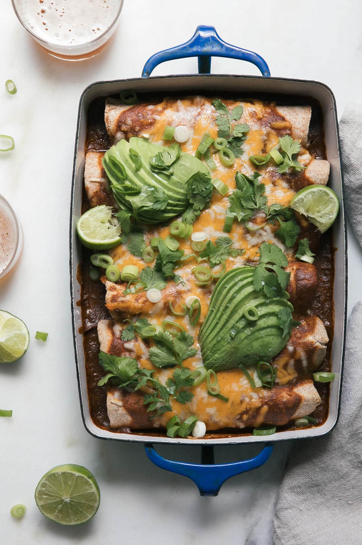 Baked vegetarian black bean enchiladas in a baking dish with lime wedges and avocado.