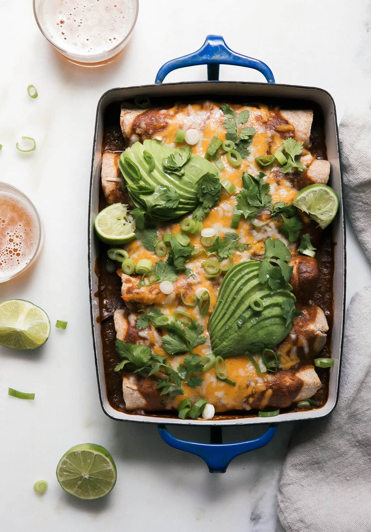 Vegetarian black bean enchiladas topped with sliced avocado and lime wedges in a baking dish.