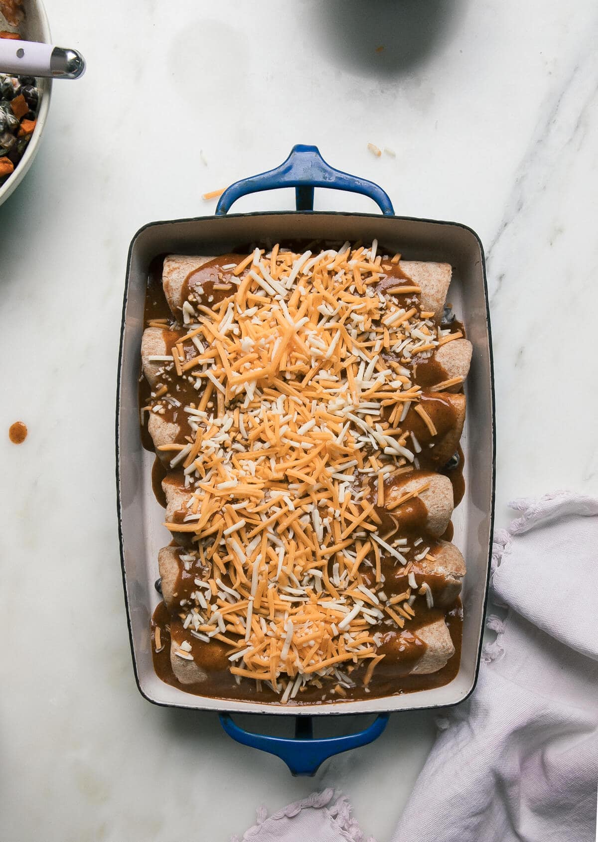Unbaked enchiladas topped with enchilada sauce and shredded cheese.
