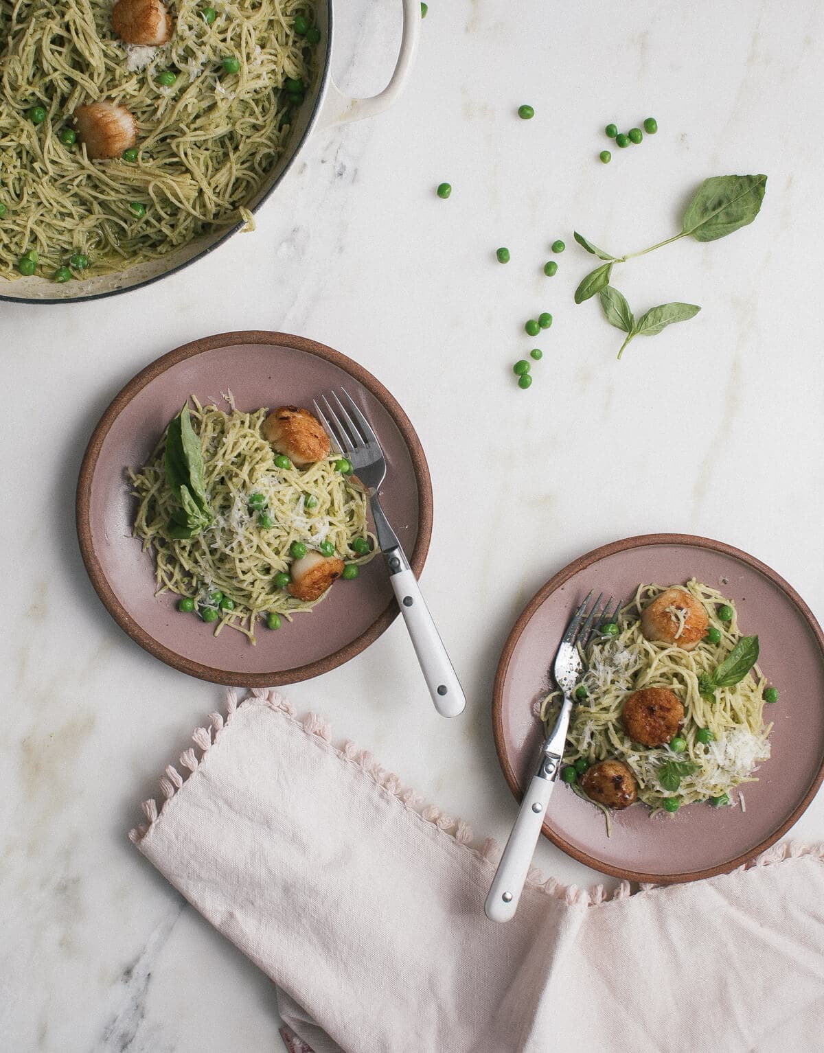 Pea pesto pasta with brown butter scallops on a plate with forks.