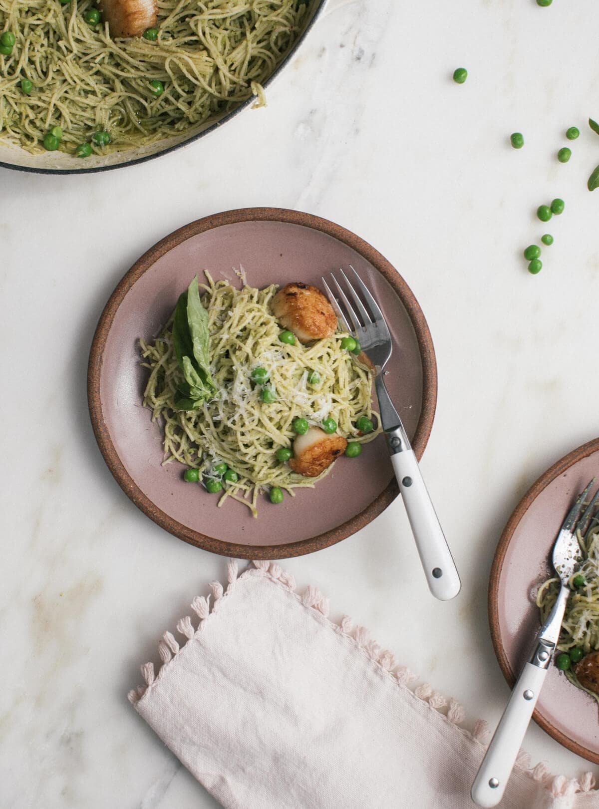 Overhead image of pea pesto pasta with brown butter scallops on a plate with peas and a fork. 