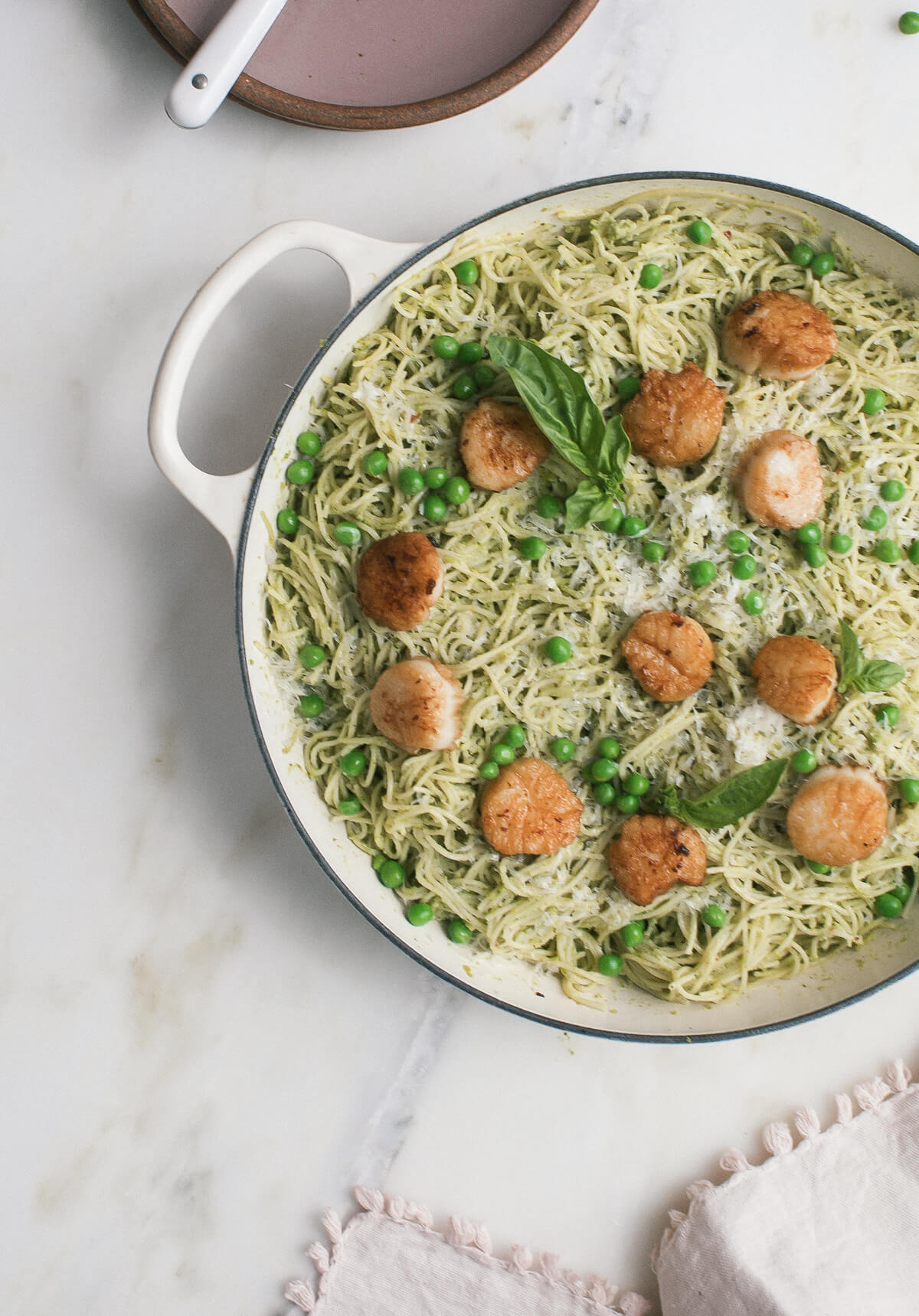 A pot of pea pesto pasta topped with brown butter scallops and fresh basil.