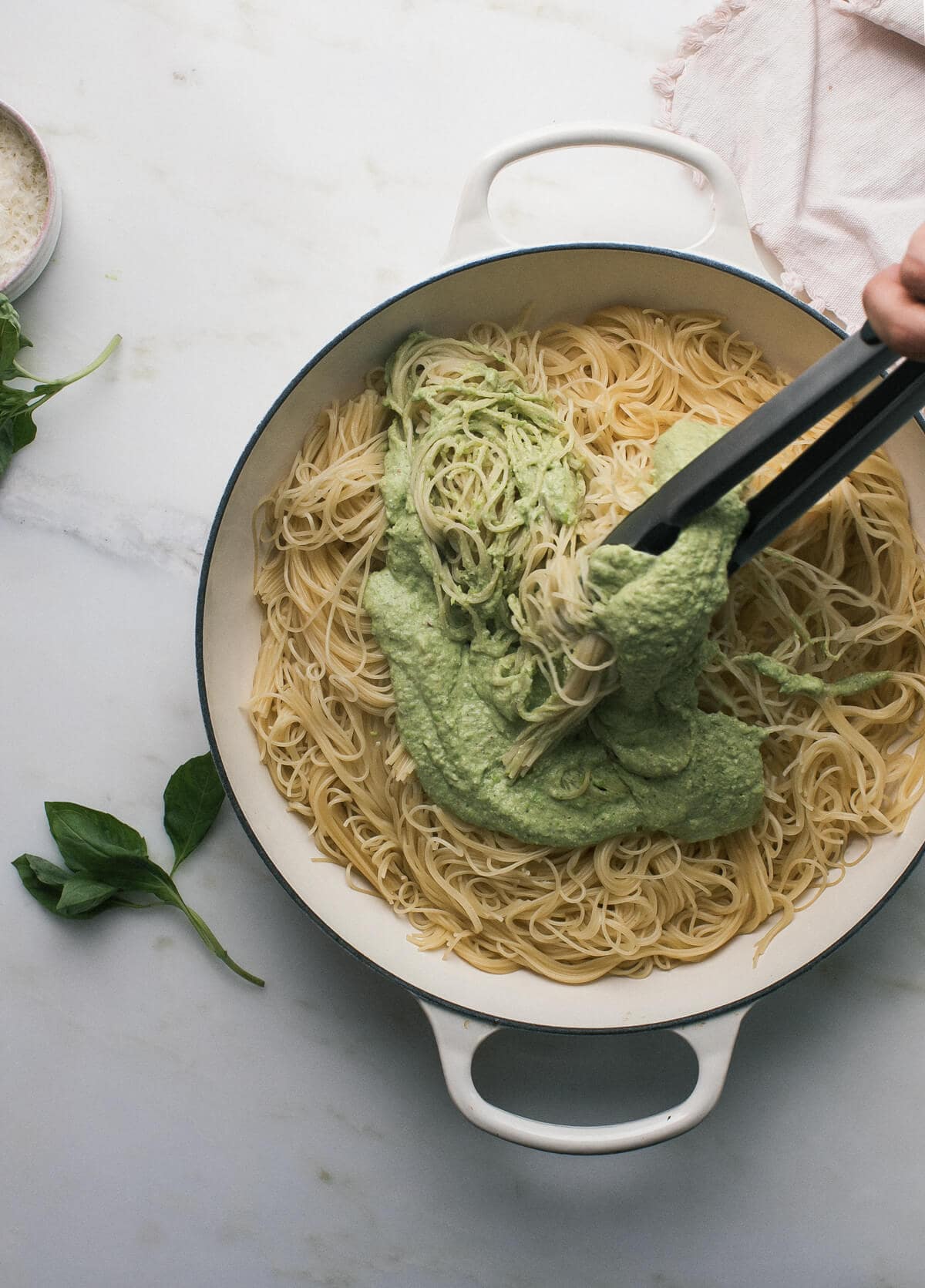 Pasta being tossed with pesto with a pair of tongs.