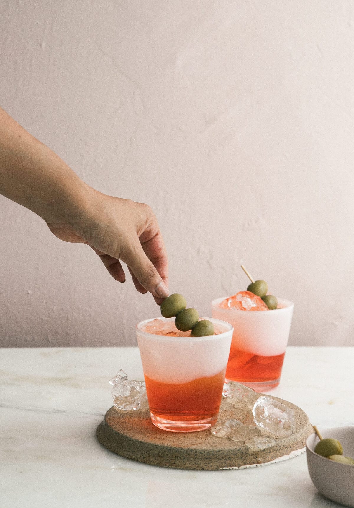 Green olives being added to cocktail. 