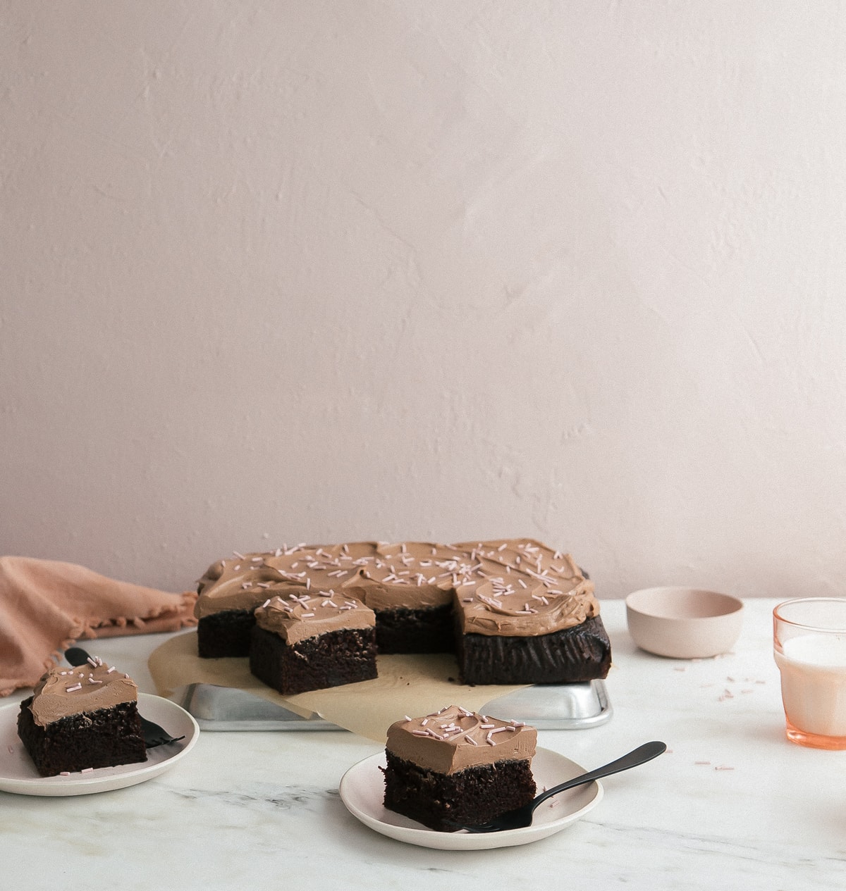 Side view of a sheet cake on a pan with slices of cake on a plate with forks.