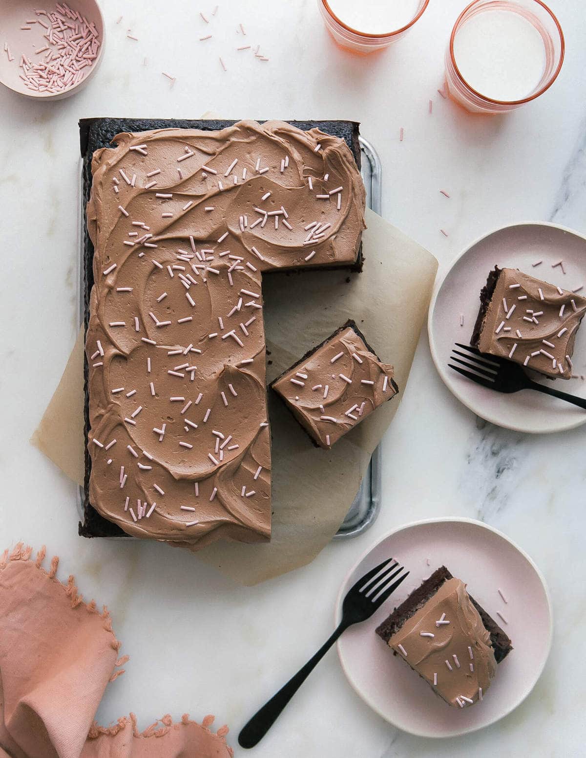 Slices of a one bowl chocolate cake cut and placed on plates topped with sprinkles.