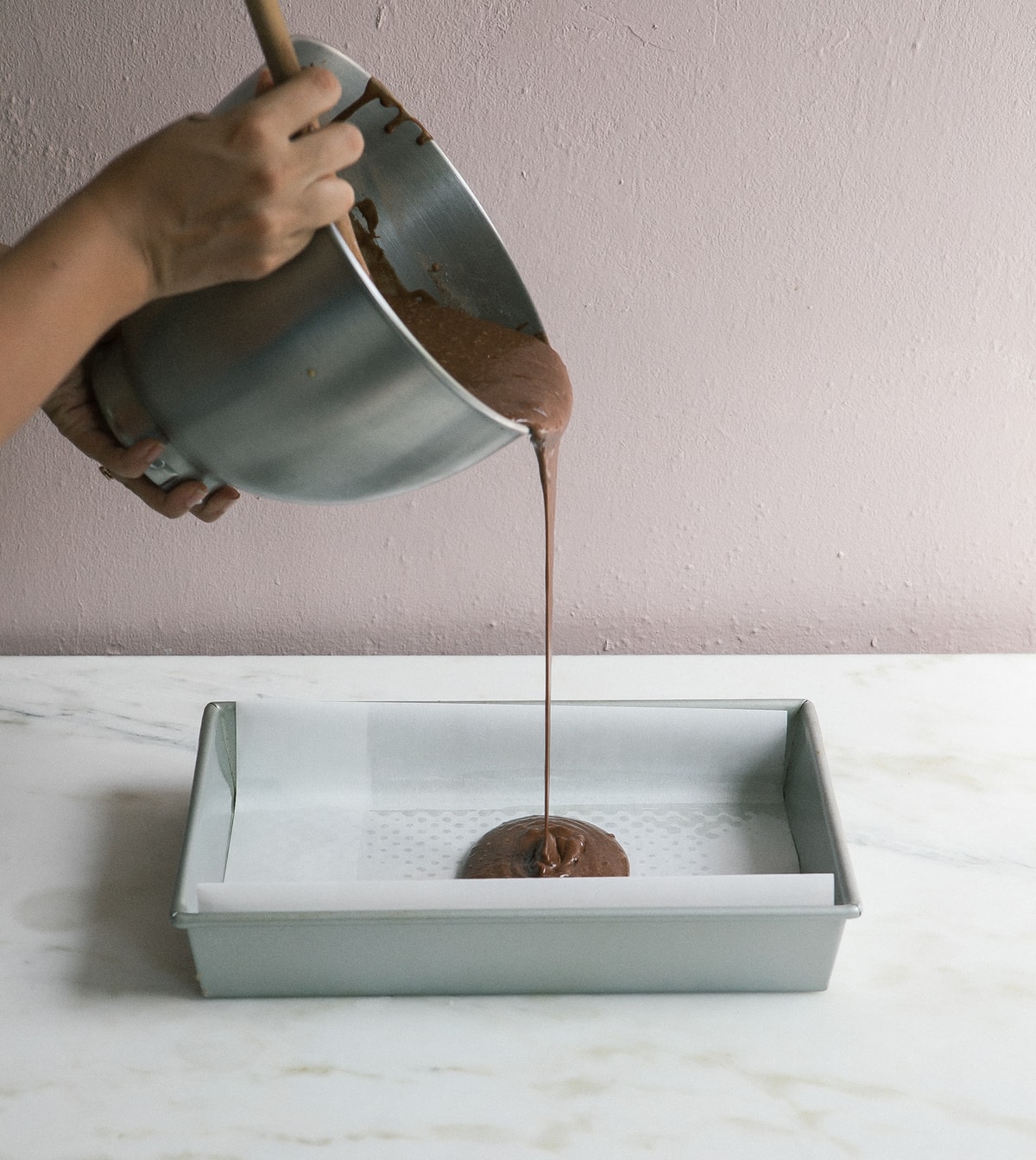 Cake batter being poured into a parchment-paper lined sheet pan.