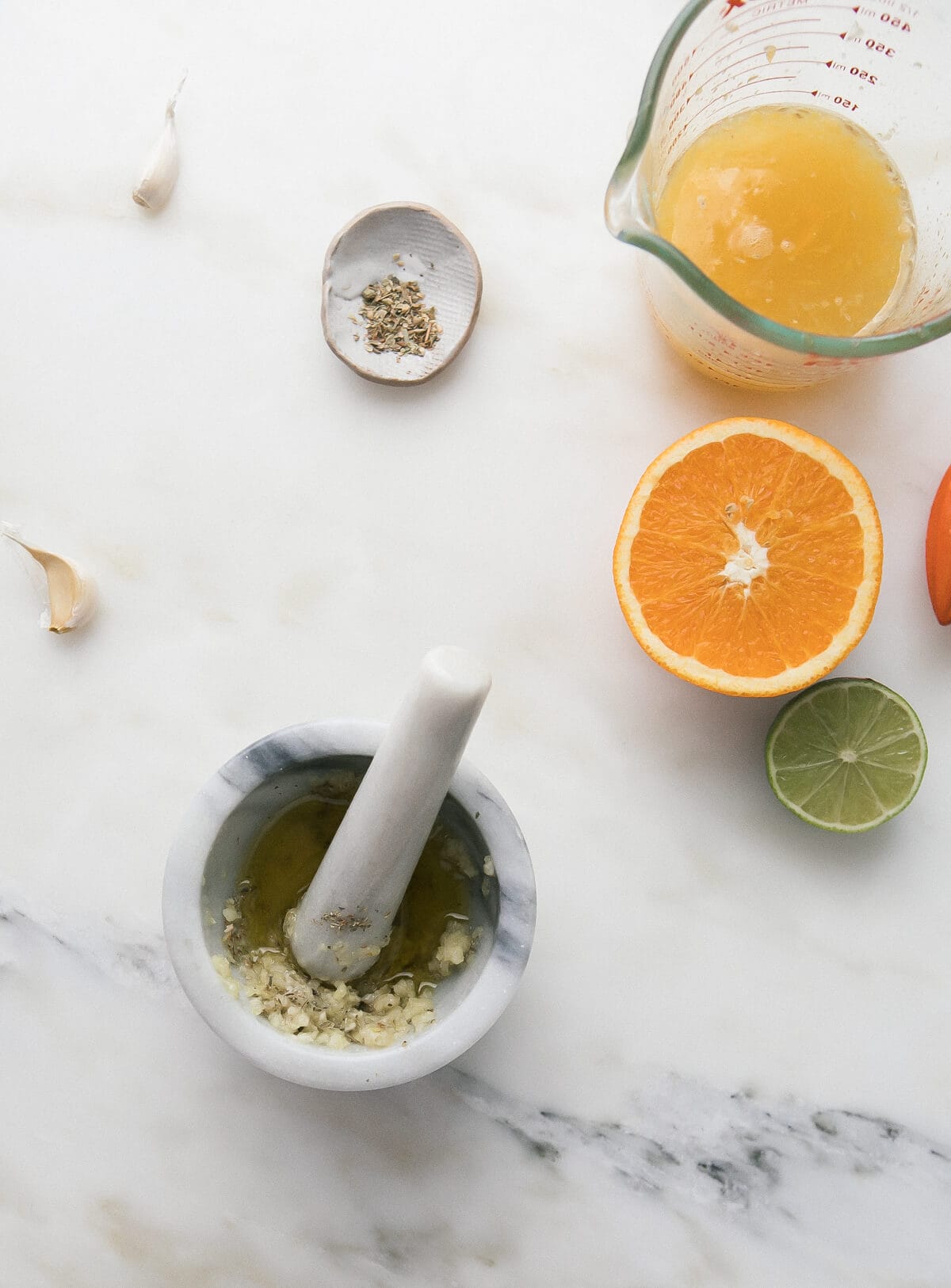 Garlic in a mortar and pestle with orange and lime halves near by.