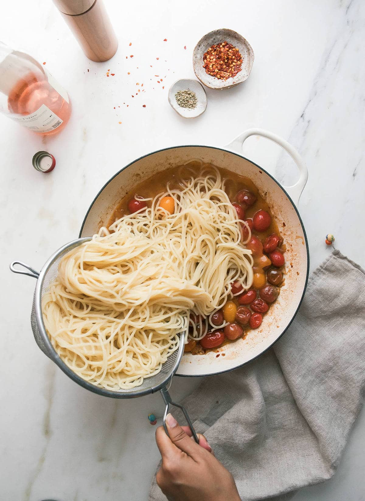 Drained pasta being poured into a pot with cooked tomatoes.