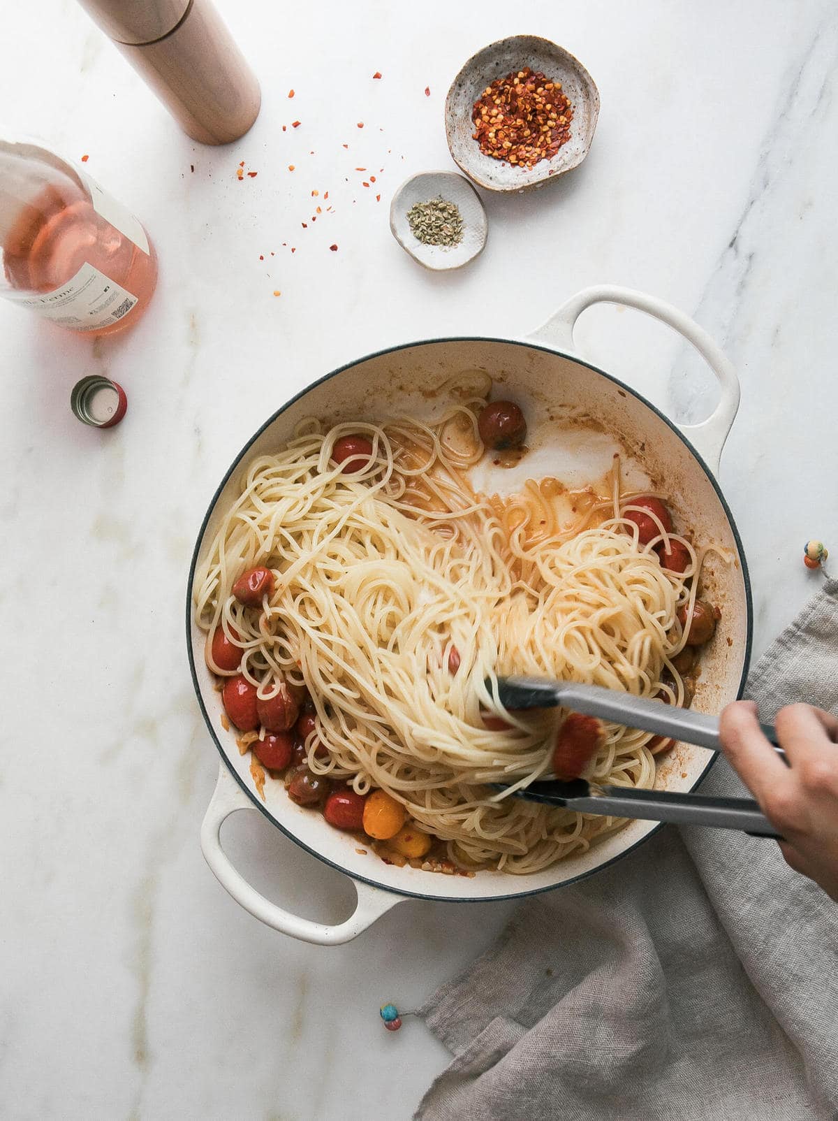 Pasta with cherry tomatoes being tossed with a pair of tongs.