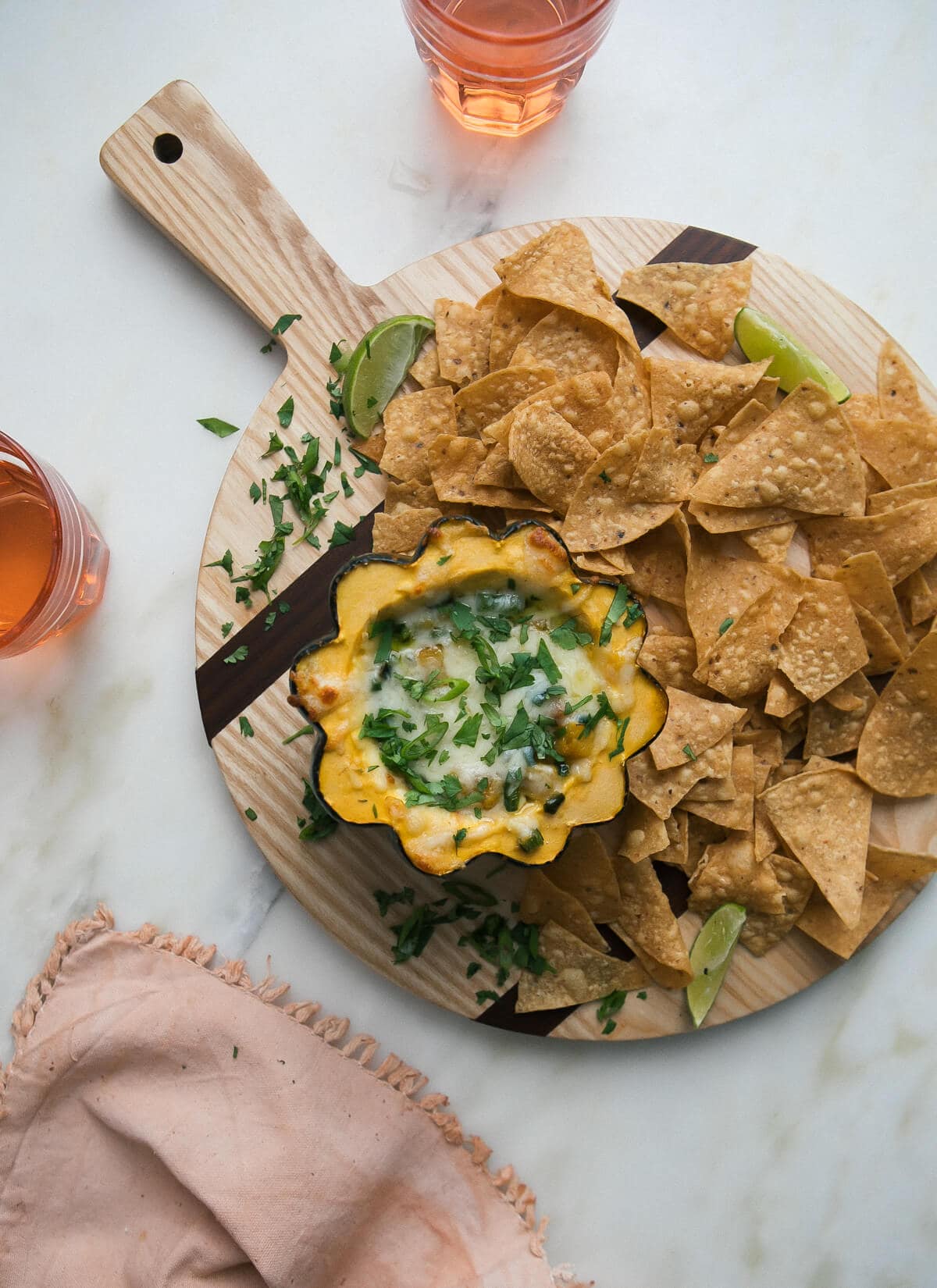 Overhead image of acorn squash pasilla chile queso fundido with tortilla chips on a wooden cutting board.