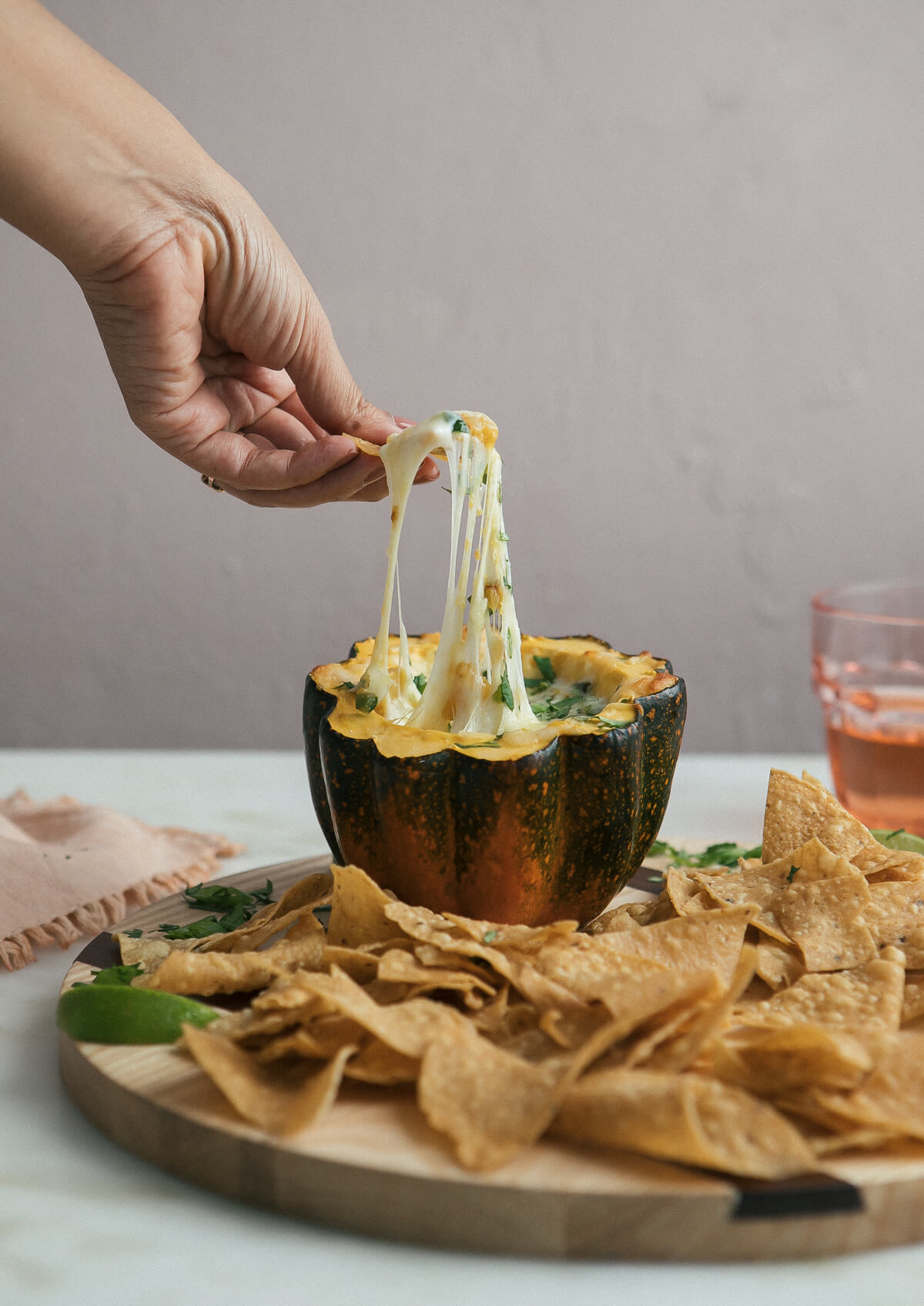 Side view of a hand scooping acorn squash pasilla chile queso fundido with a tortilla chip. 