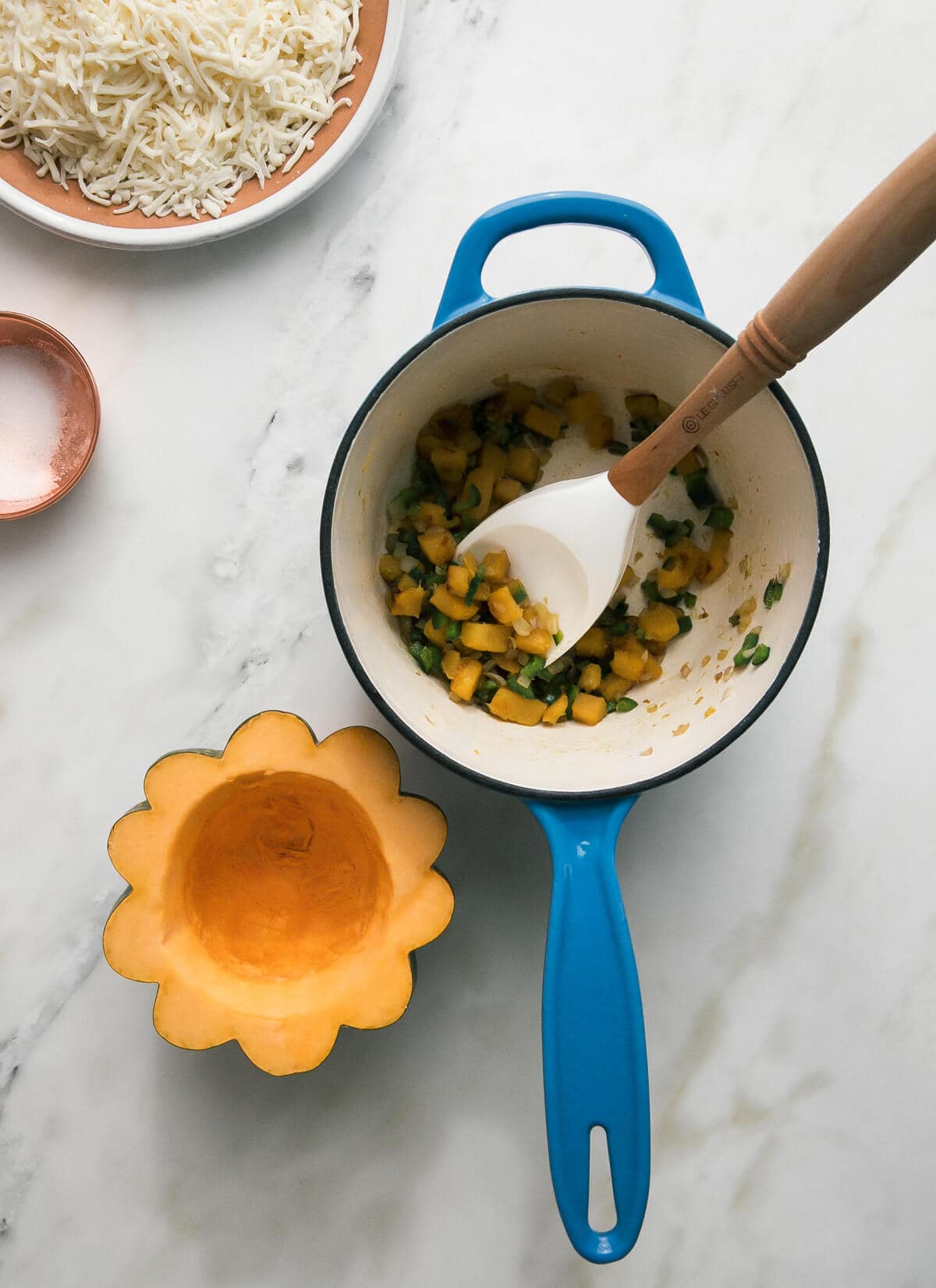 Overhead image of a cut acorn squash with squash filling in a small sauce pan.