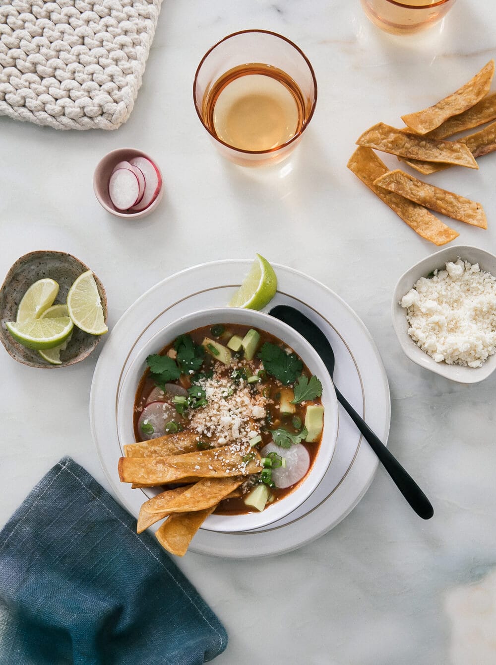 Overhead image of enchilada chicken tortilla soup in a bowl with tortilla strips and lime wedges.