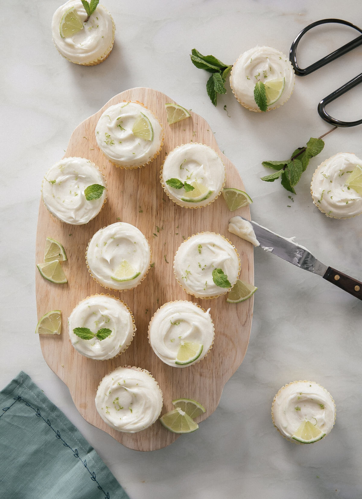 Overhead image of mojito cupcakes topped with frosting and lime slices on a counter.