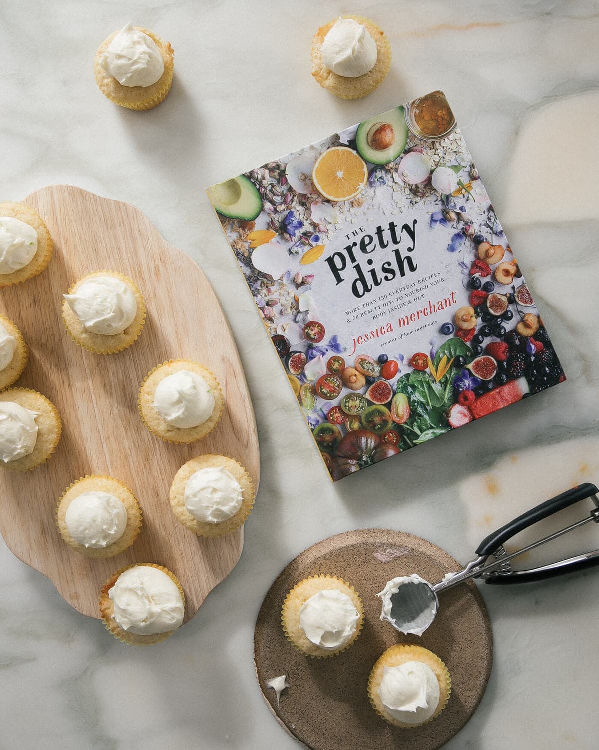 Cupcakes topped with frosting with a cookbook near by.