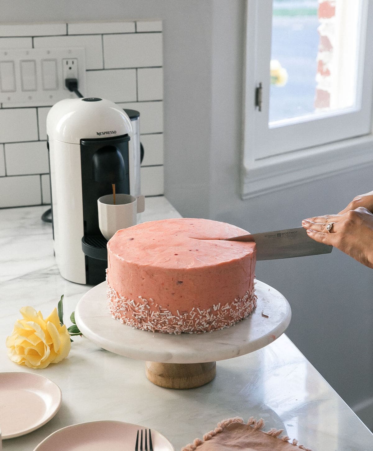 Knife cutting into a frosted corn cake with guava frosting on a cake stand. 