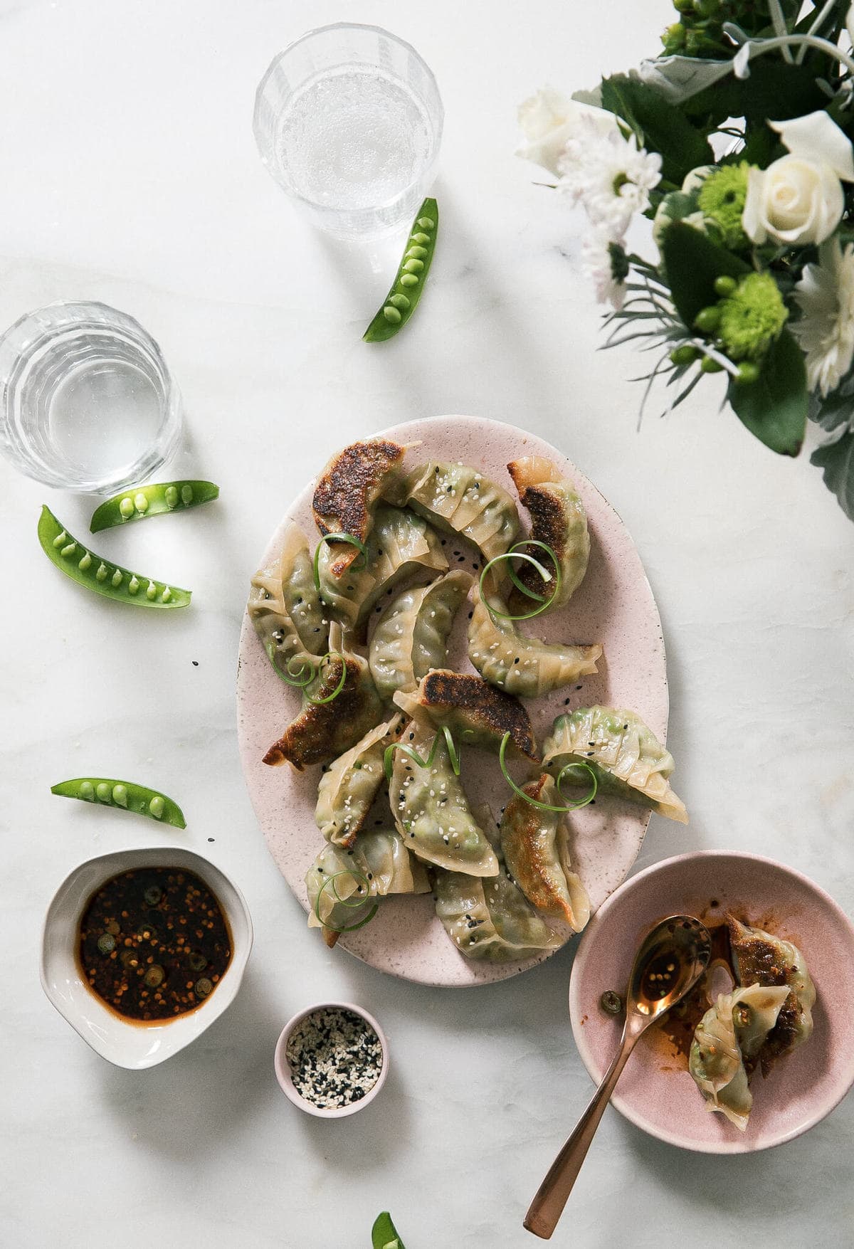 Vegetarian Potstickers on a serving platter with fresh peas and a dipping sauce nearby.