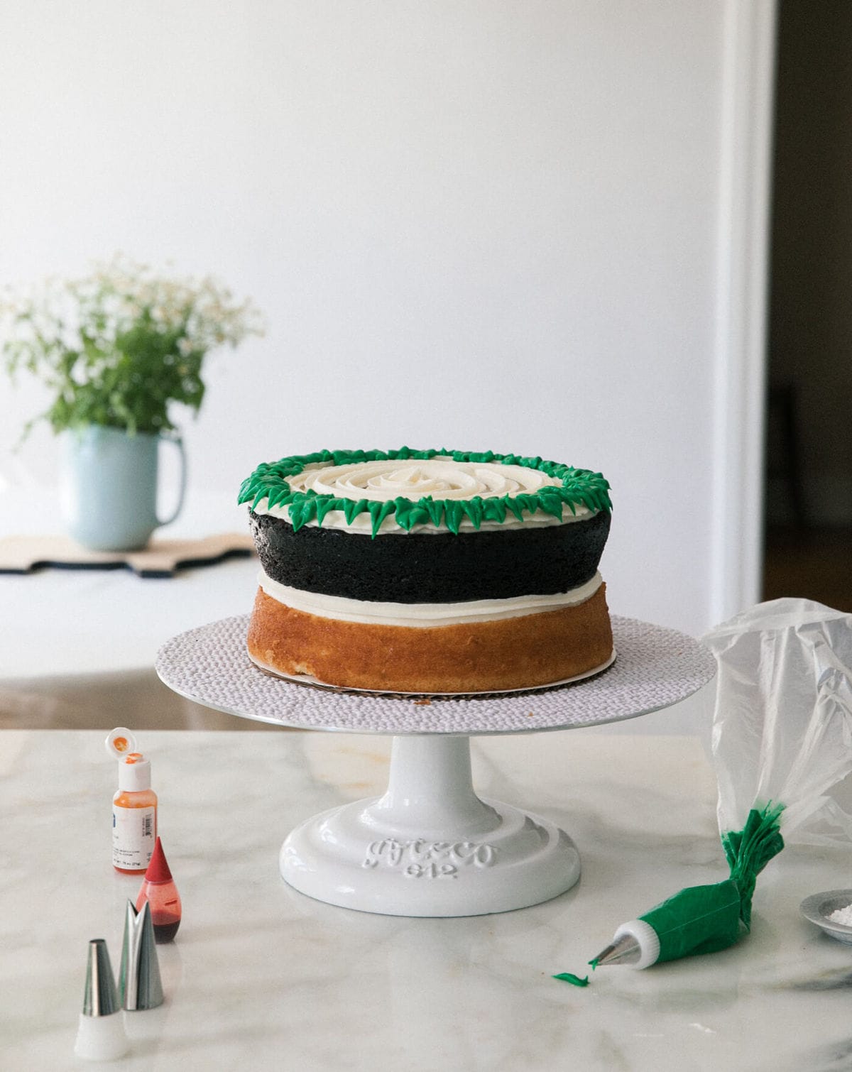 Process shot of a cake being decorated on a cake stand.