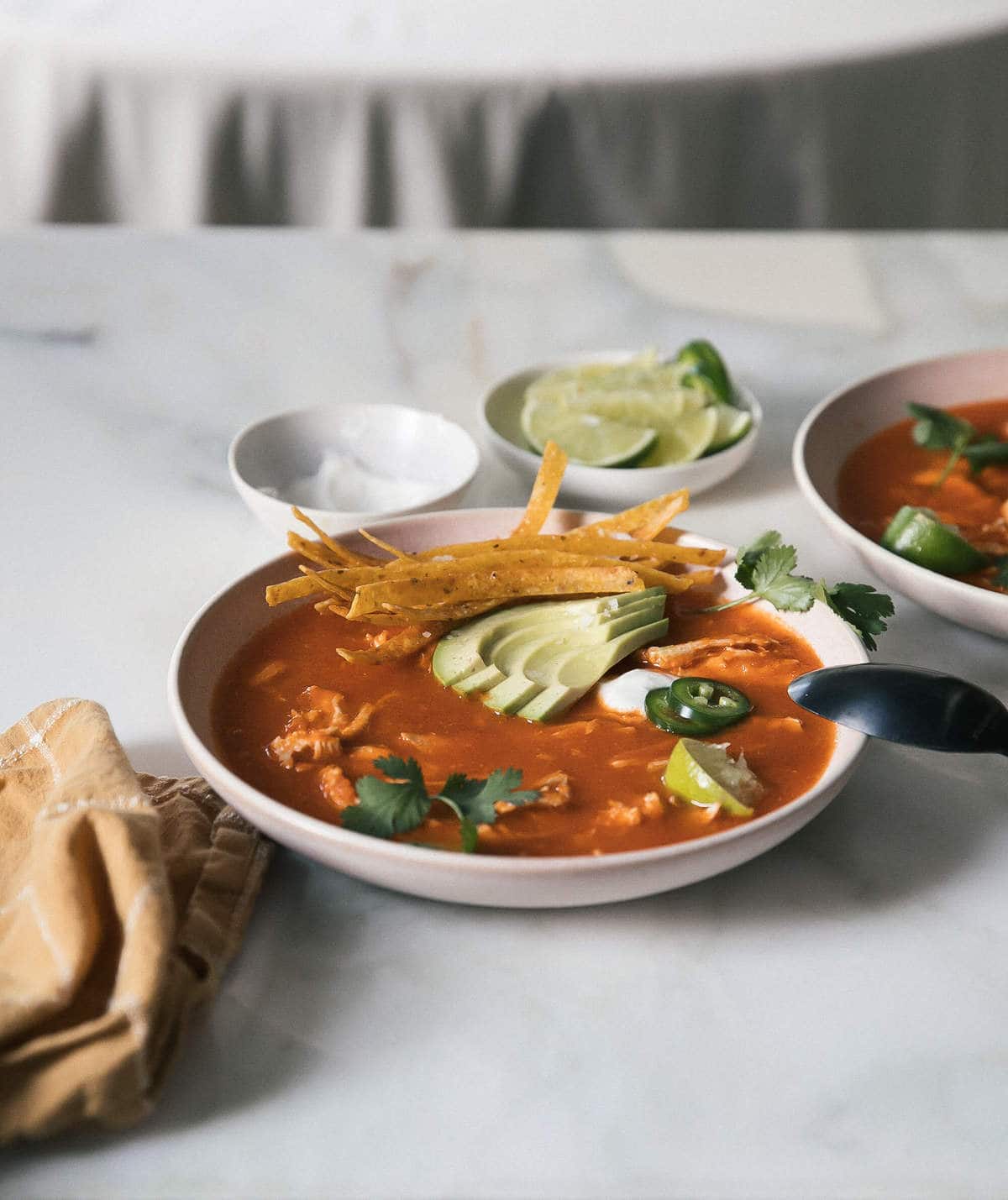 Instant pot chicken tortilla soup in a bowl topped with sliced avocado and crispy tortilla strips.