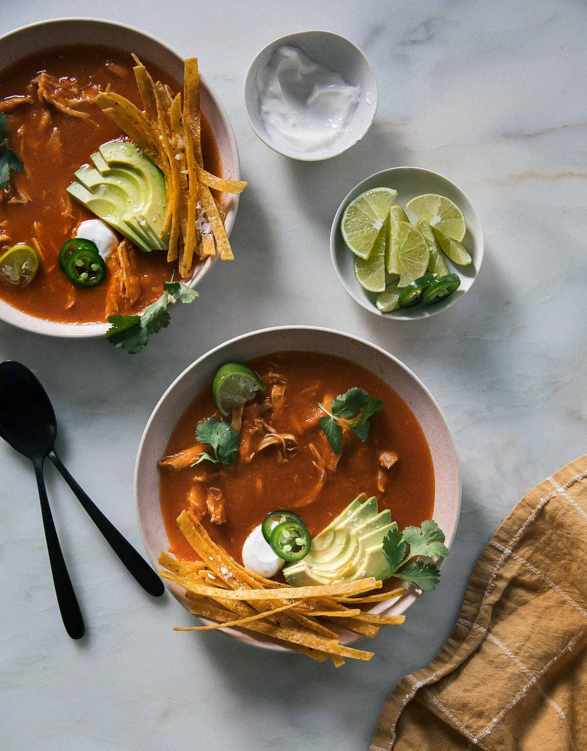 Close up image of instant pot chicken tortilla soup in a bowls with spoons and lime wedges near by.