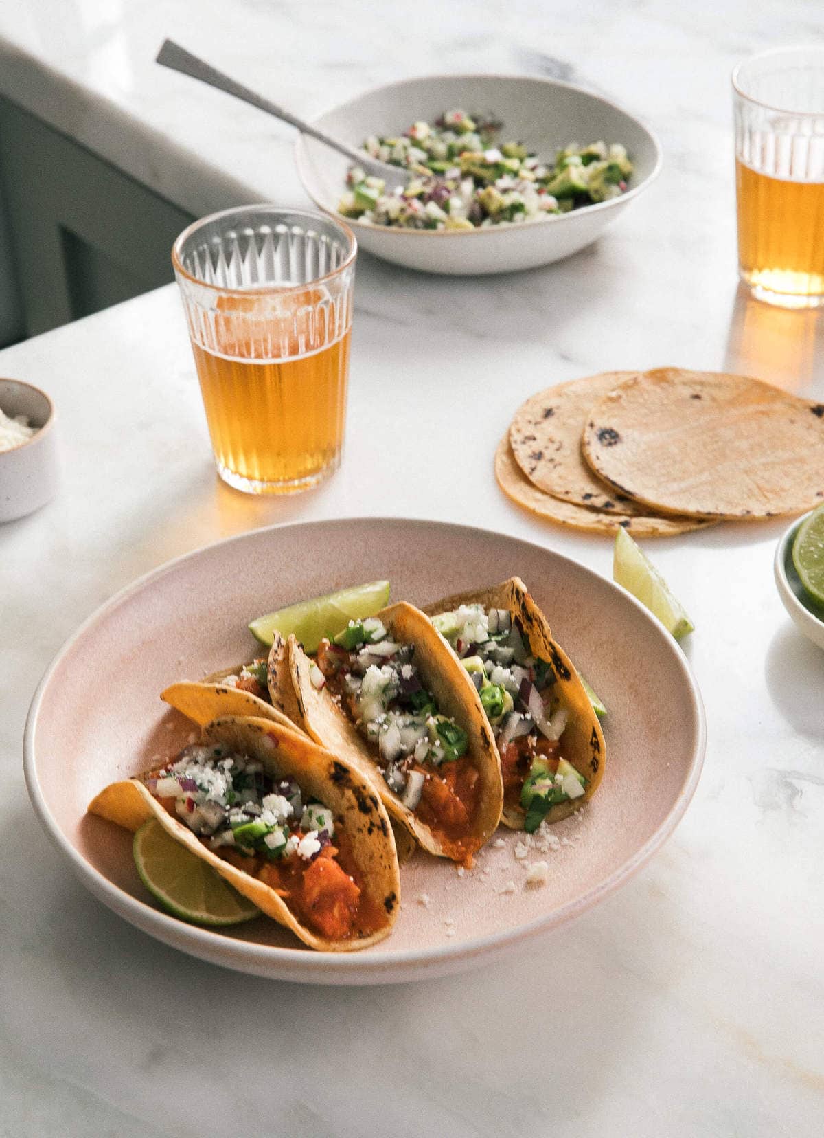 Side view of tacos on a plate with lime wedges and a beer near by.