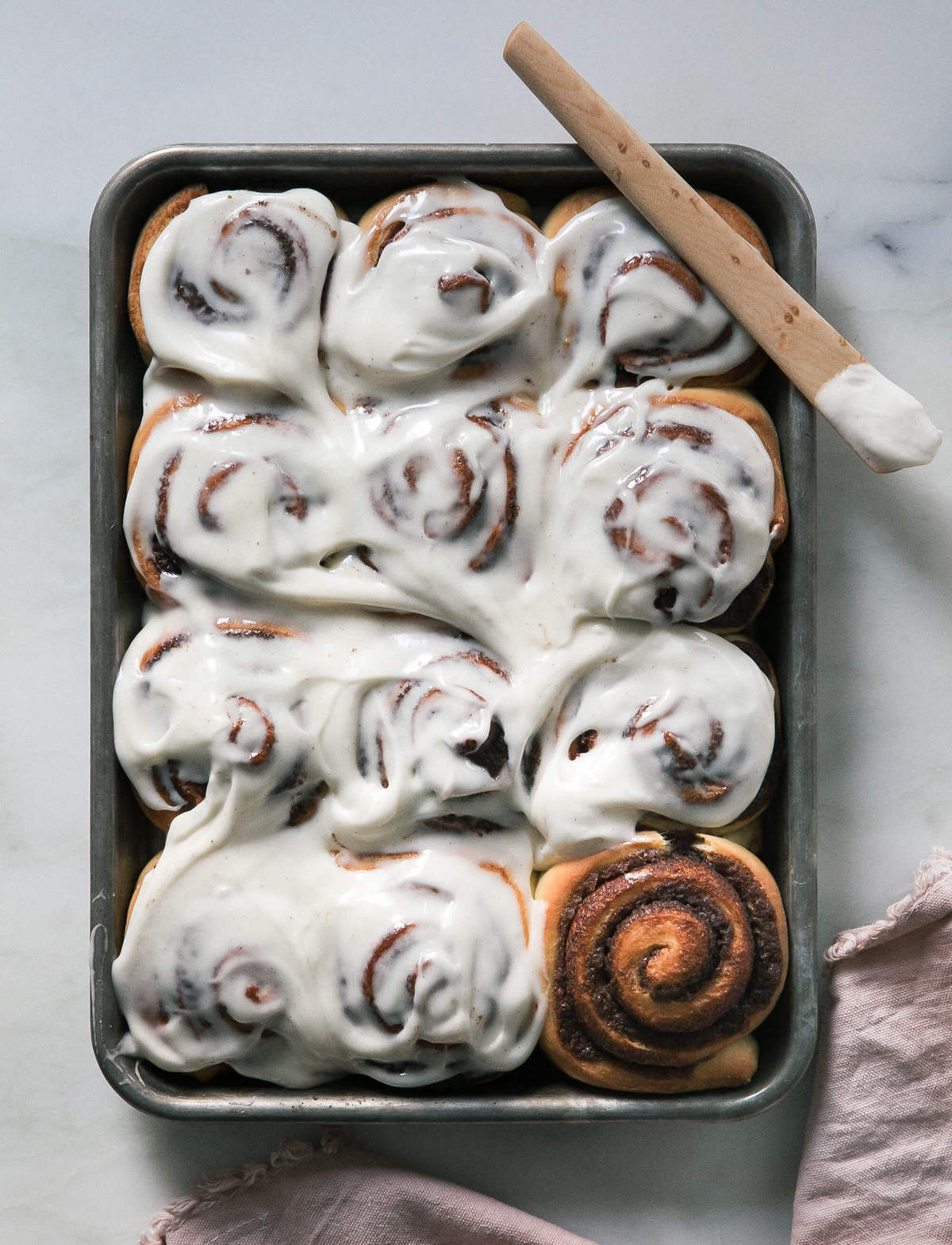 warm cinnamon rolls with frosting being smothered on