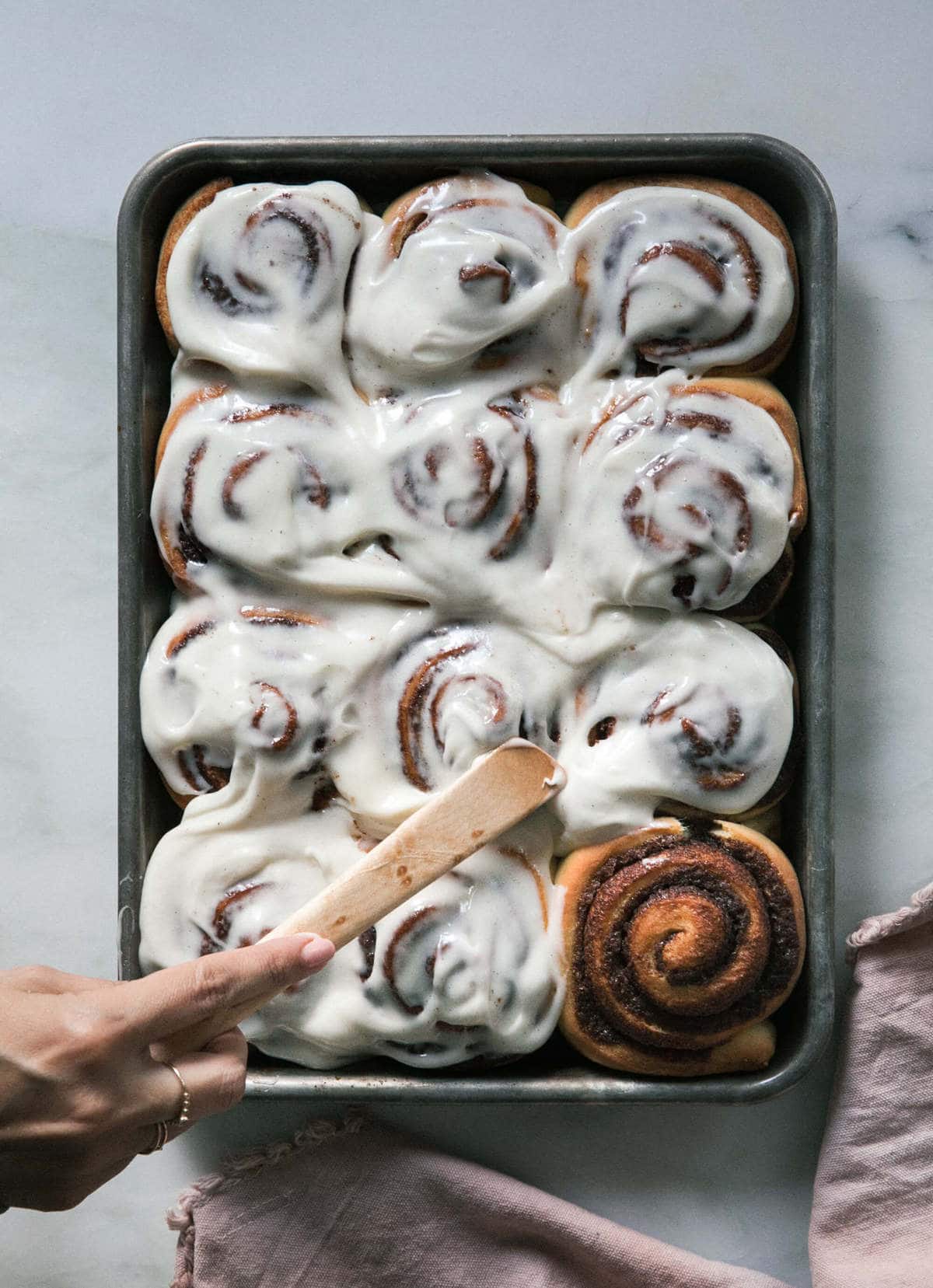 warm cinnamon rolls with frosting being smothered on