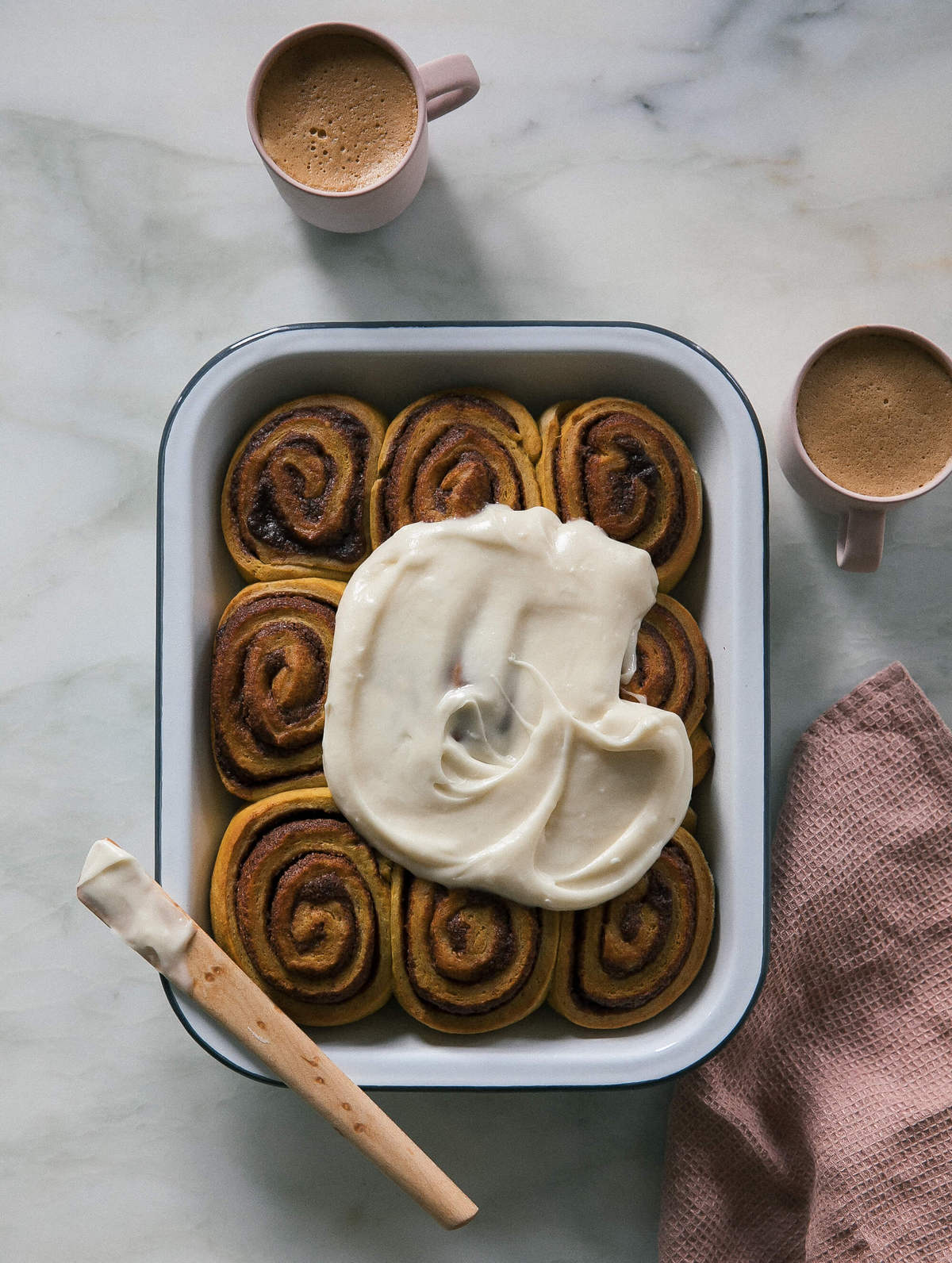 Pumpkin cinnamon rolls in baking dish with maple cream cheese frosting on top. 