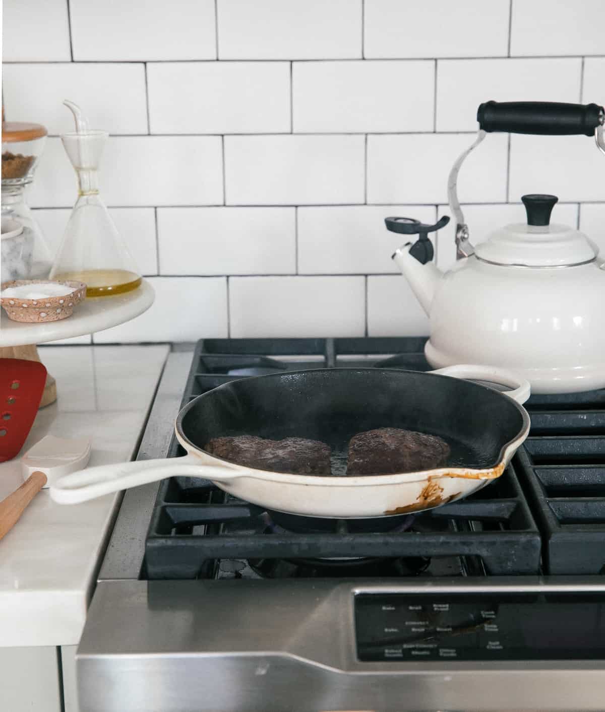 Burger patty in a cast iron skillet on the stove.