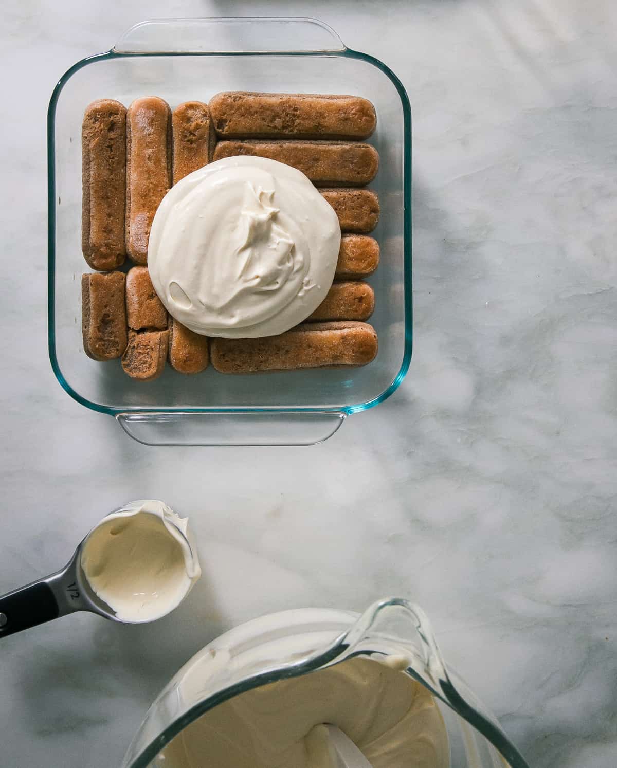 Lady fingers being layered with sweet mascarpone mixture in baking dish. 