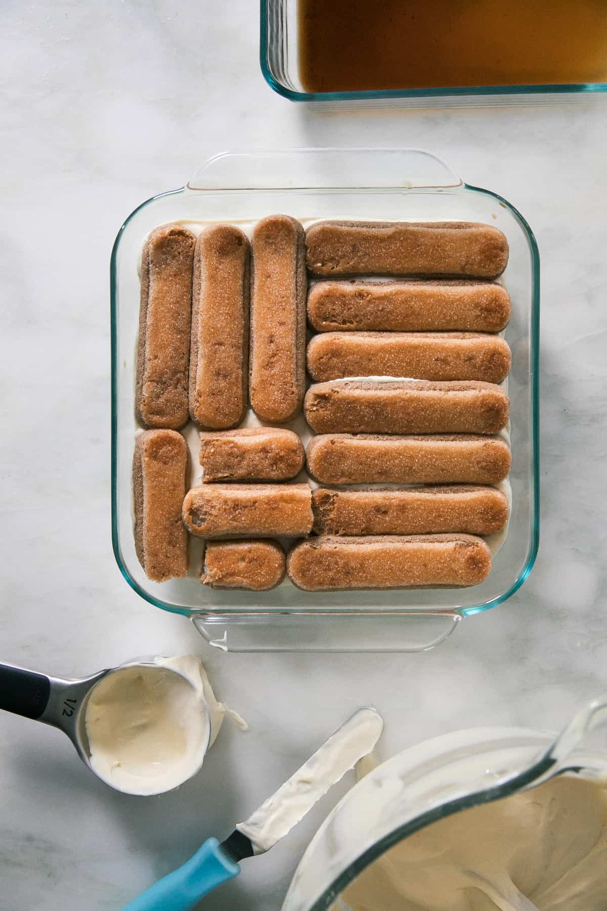 Lady fingers being layered with sweet mascarpone mixture in baking dish. 