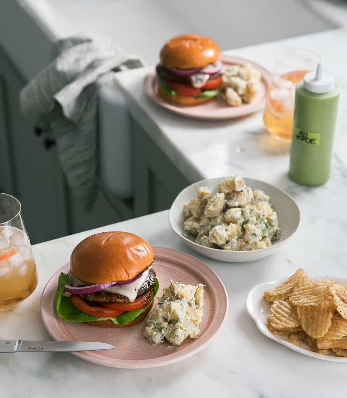 Grilled Portobello Mushroom Burgers on a plate with chips and potato salad. 