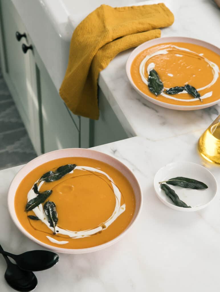 Bowls of acorn squash soup with a drizzle of creme fraiche on top with crispy sage. 