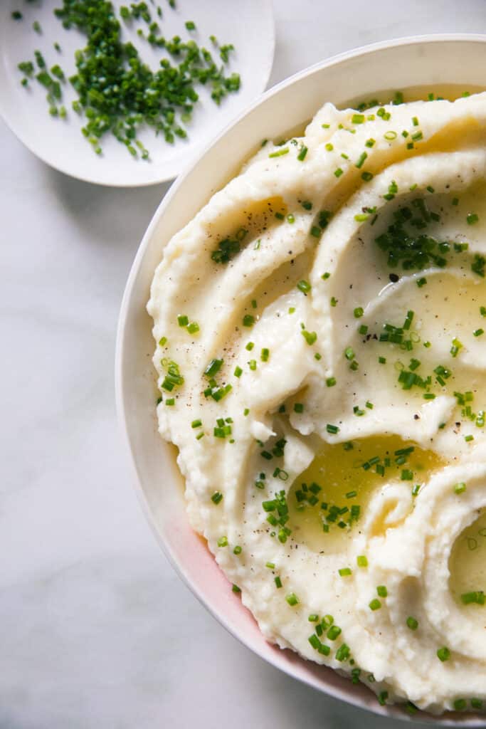 Creamy mashed potatoes on a bowl with melted butter and chives on top. 