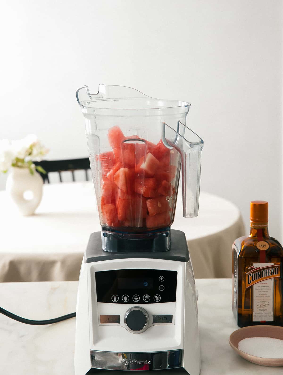 Watermelon in blender with ingredients all around.
