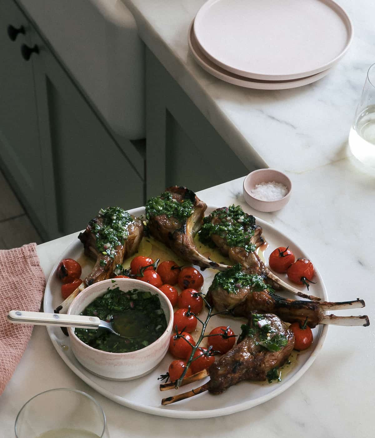 Lamb chops on plate with chimichurri and roasted tomatoes. 