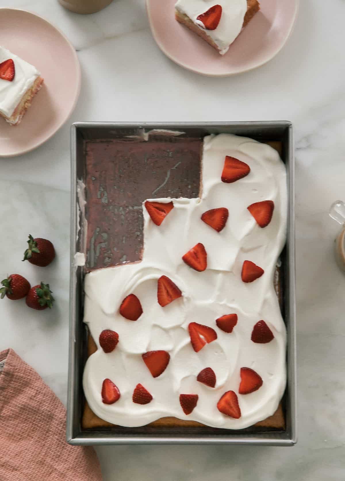 Strawberry Tres Leches Cake on counter with slices taken out. 