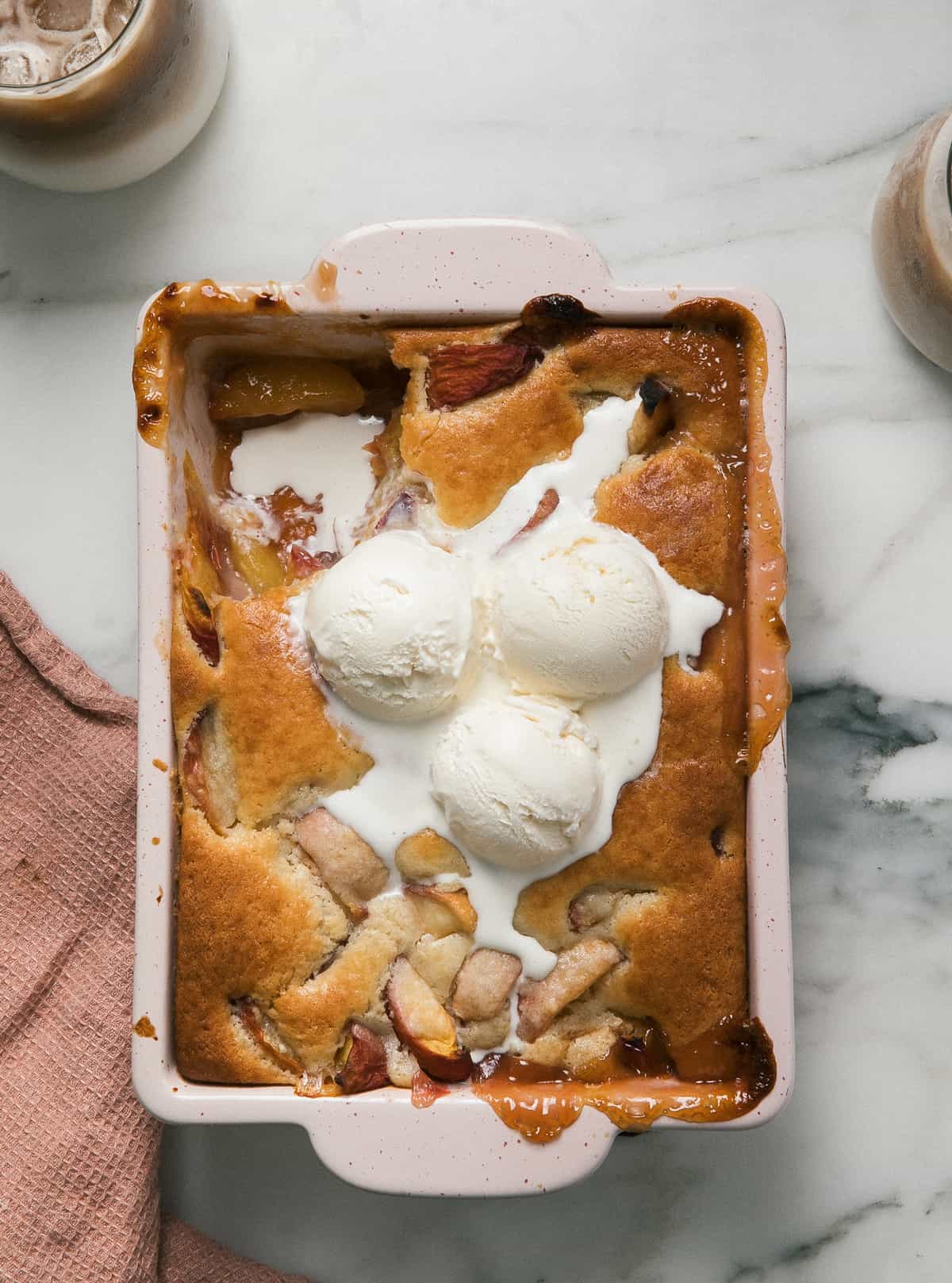 Easy Peach Cobbler in baking dish with ice cream. 