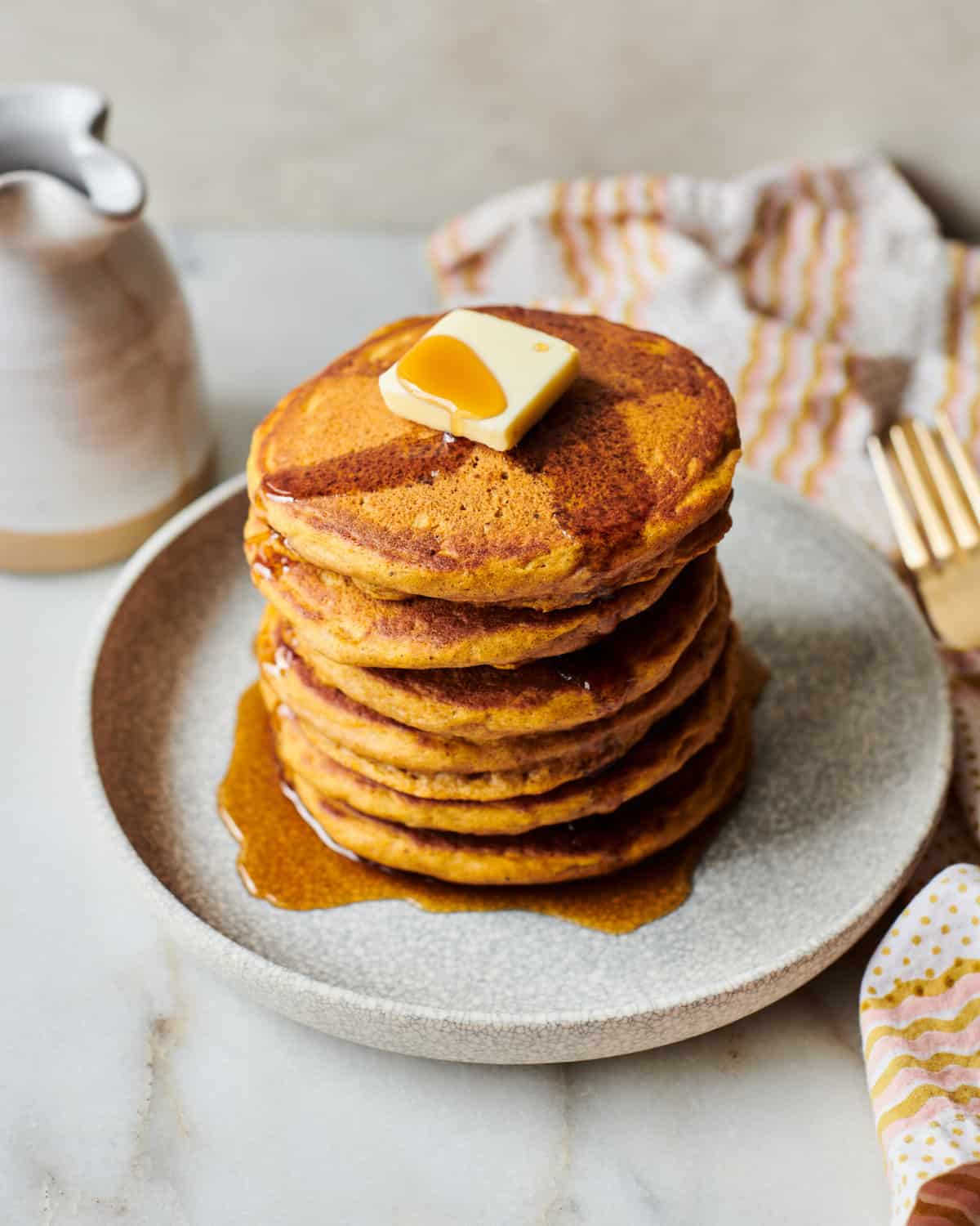 Pumpkin Pancakes stacked on a plate with syrup and butter. 