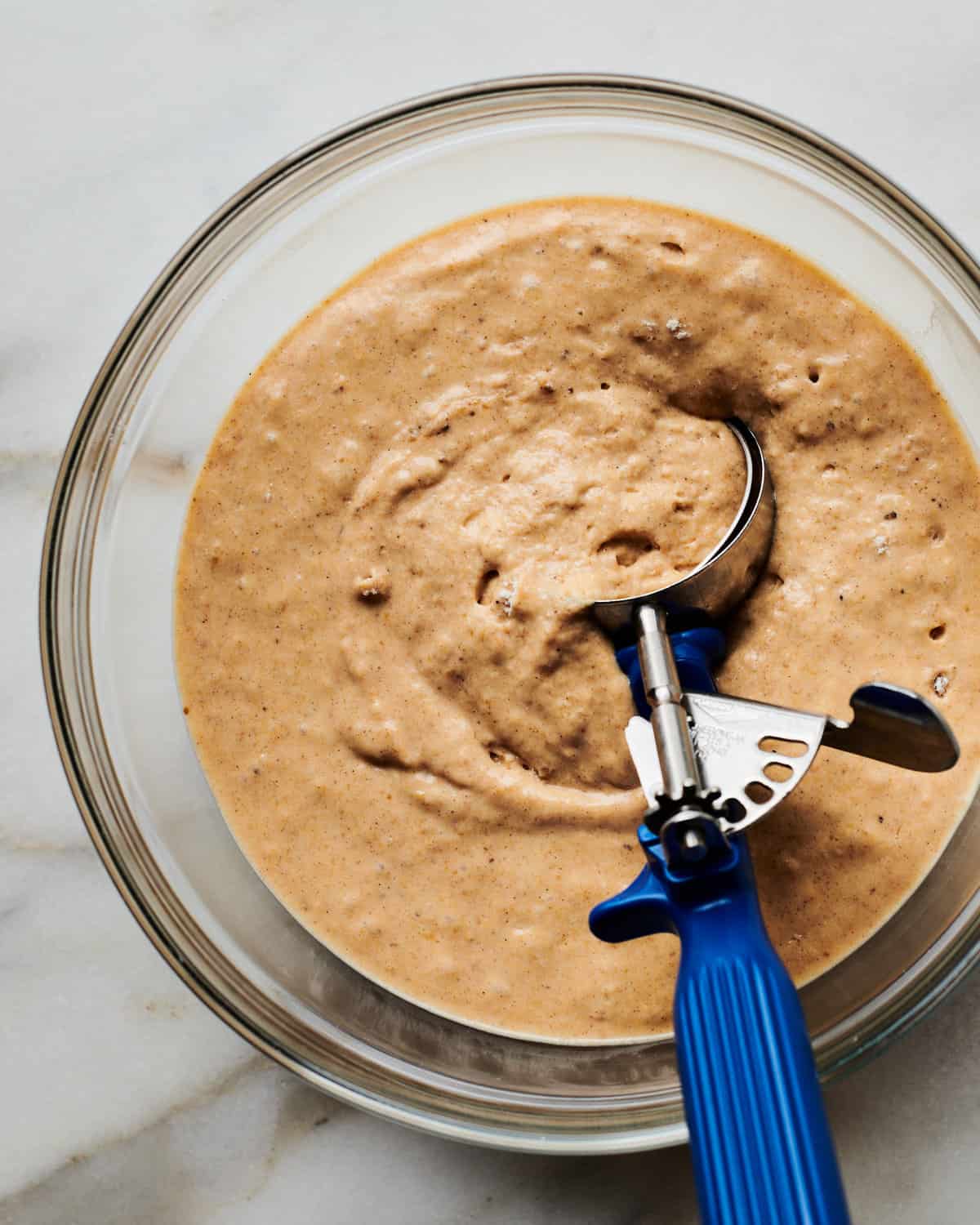 Pancake batter in a bowl with an ice cream scoop. 