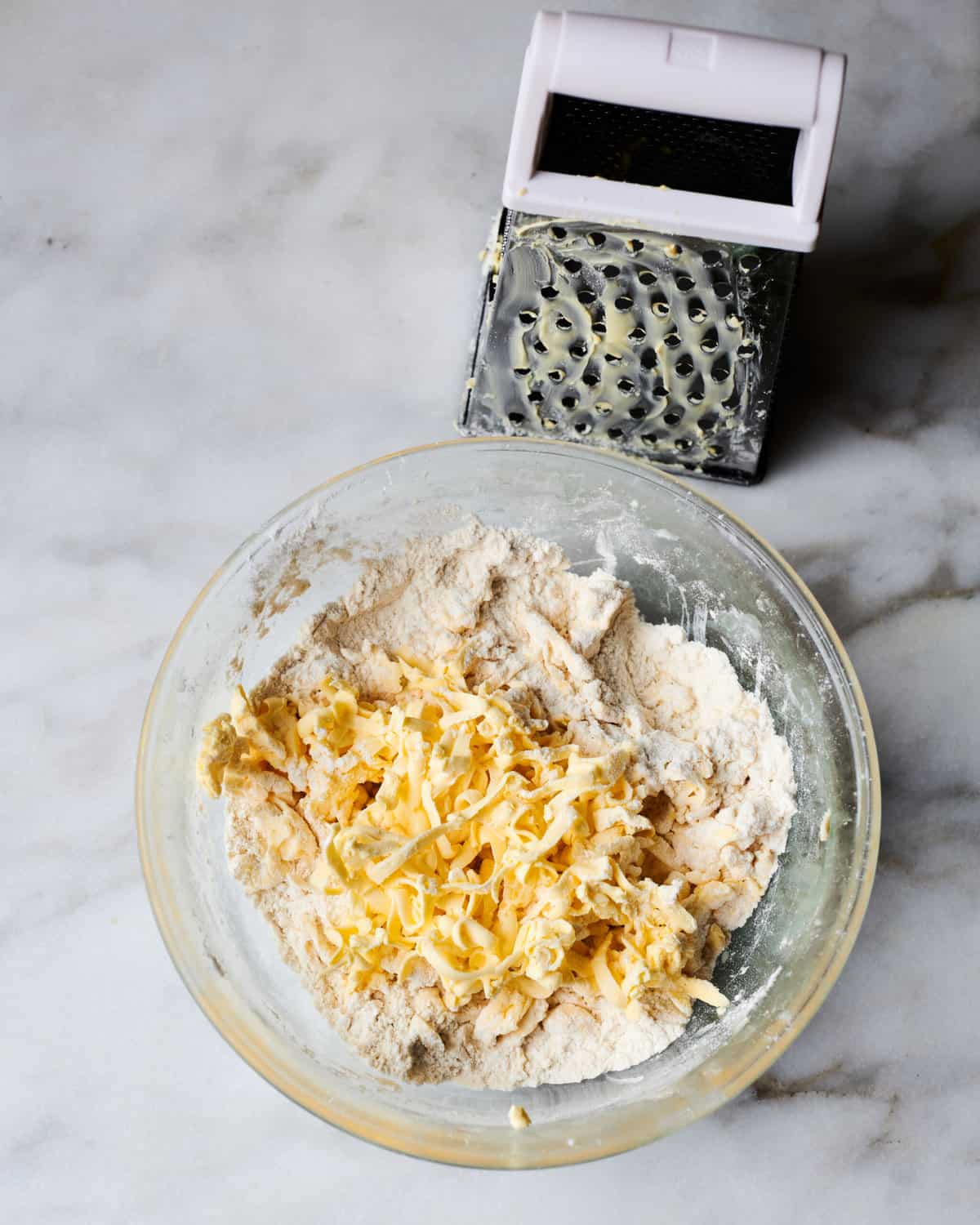 butter being grated in bowl on top of flour.
