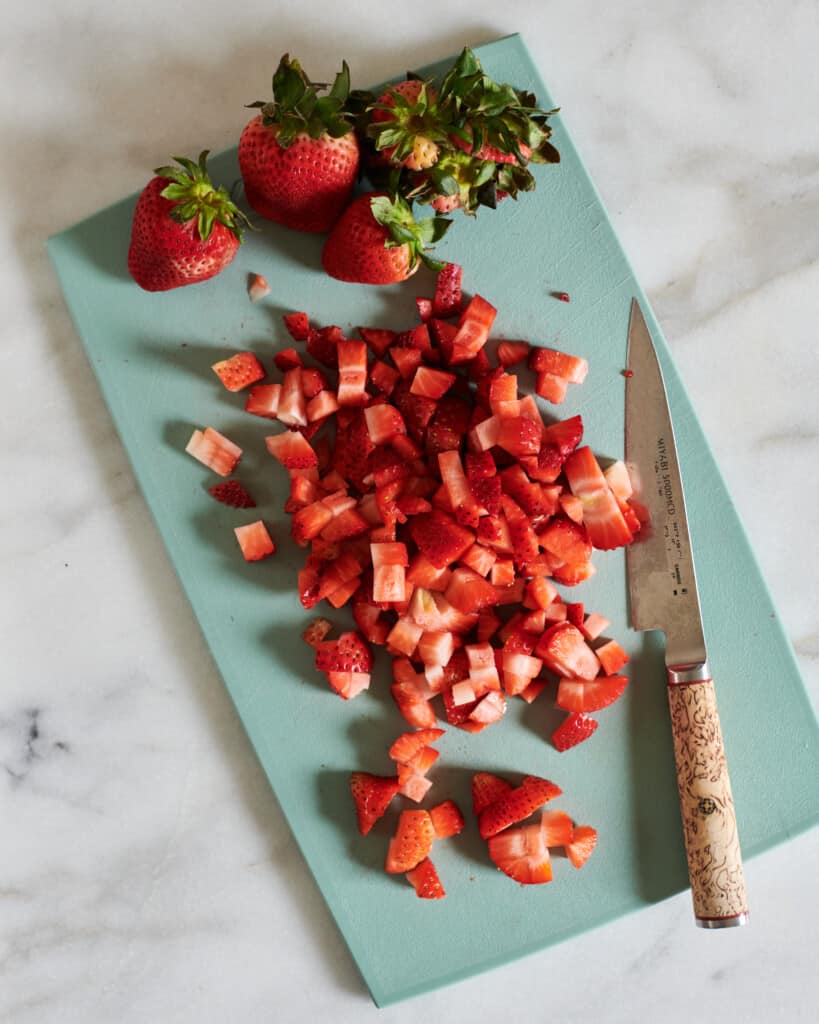 Chopped strawberries on a cutting board with a knife