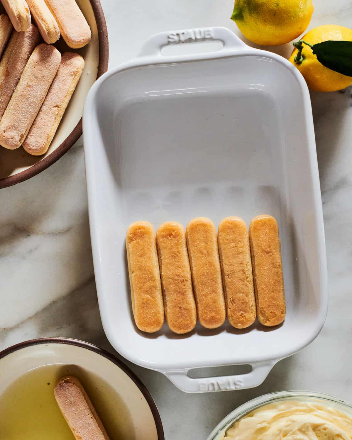 Lady fingers being added to baking dish.