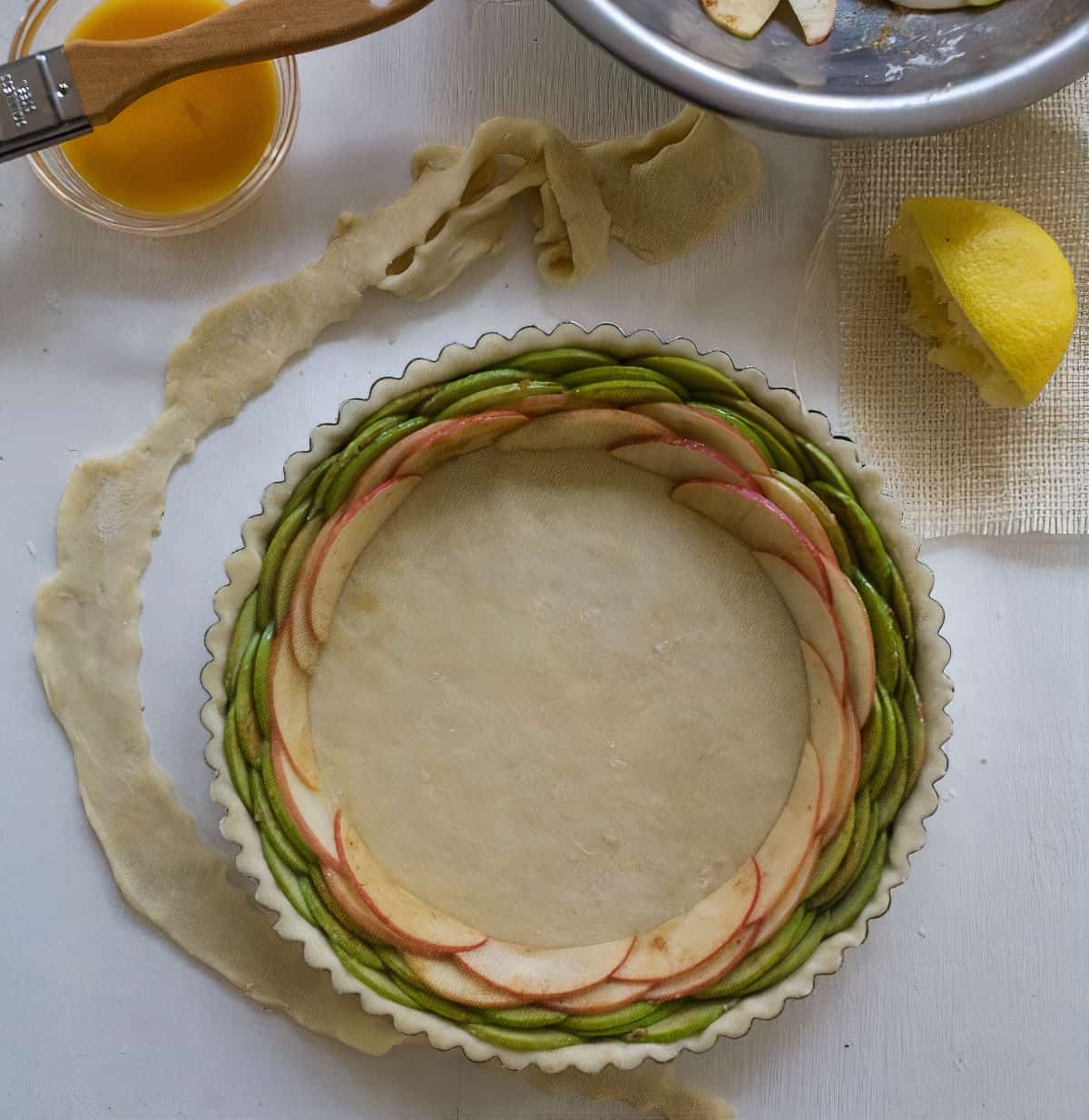 Pie being assembled. Slices of apples all around.