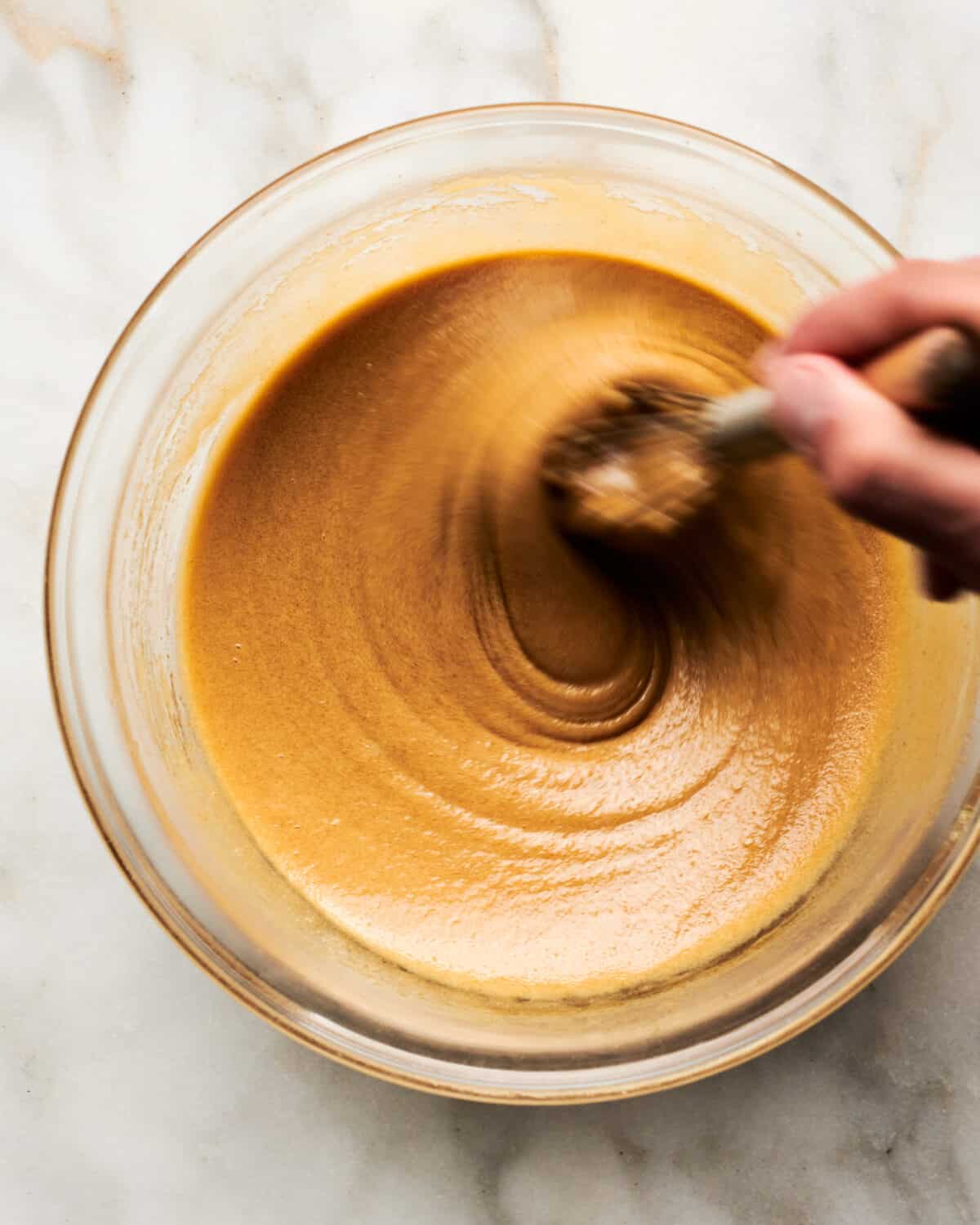 Butter and eggs being mixed in bowl with whisk.