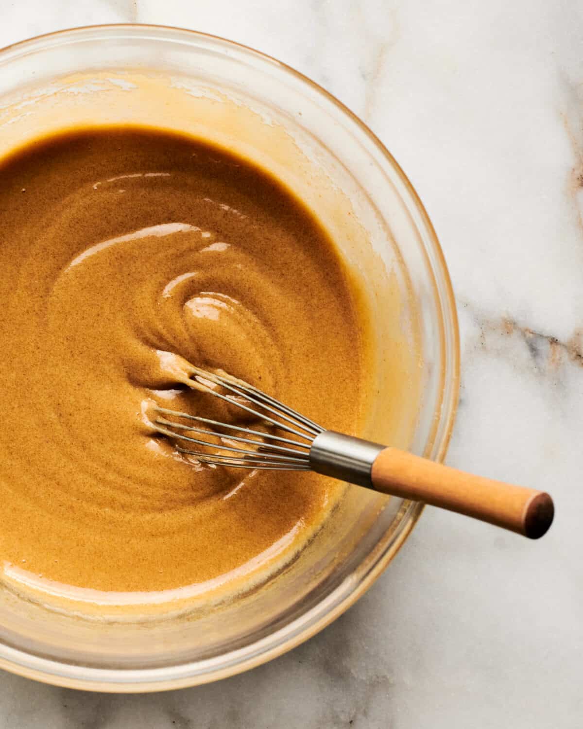 Butter and eggs being mixed in bowl with whisk.